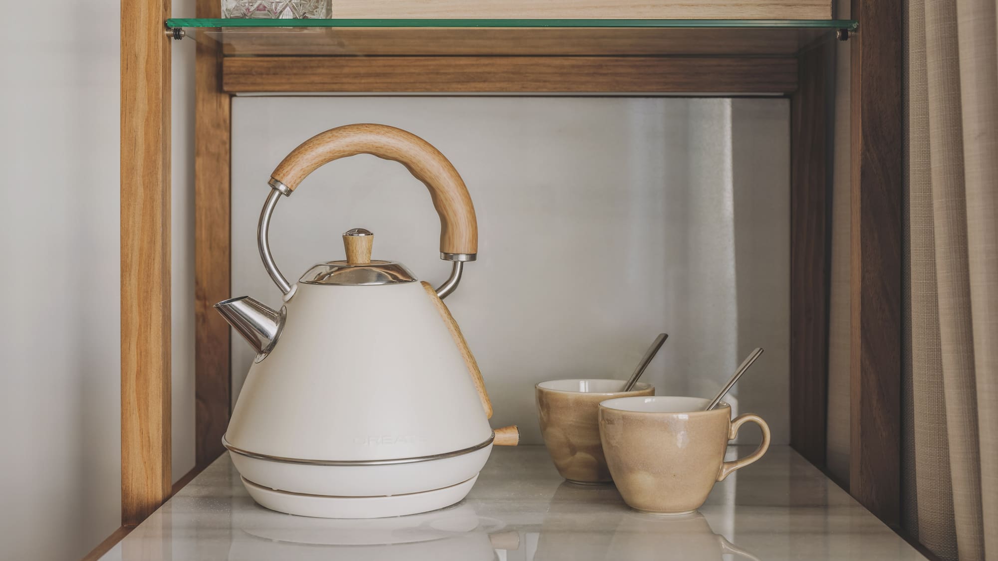 Cream electric kettle, wooden handle, and two mugs on a marble counter.