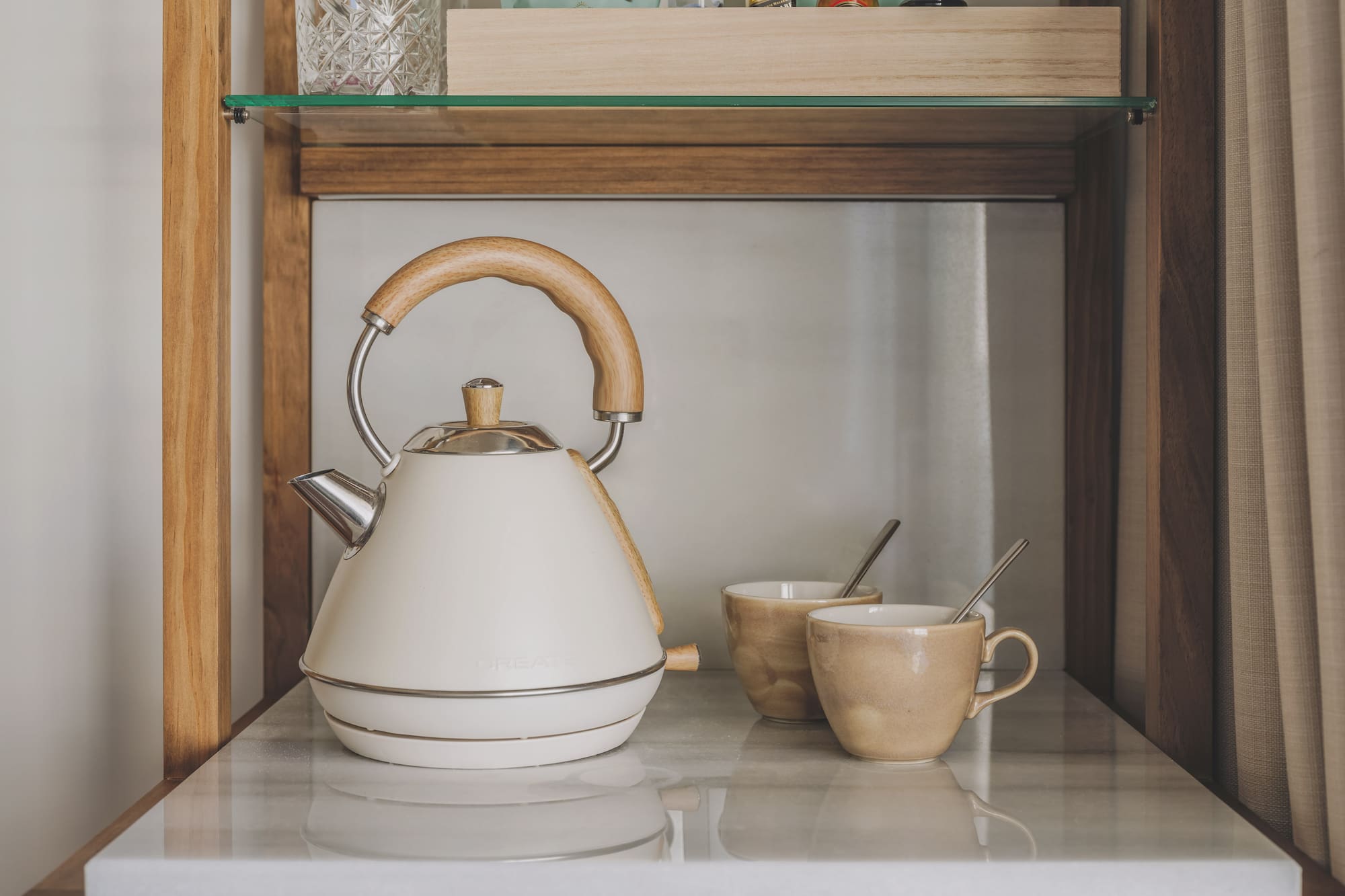 Cream electric kettle, wooden handle, and two mugs on a marble counter.