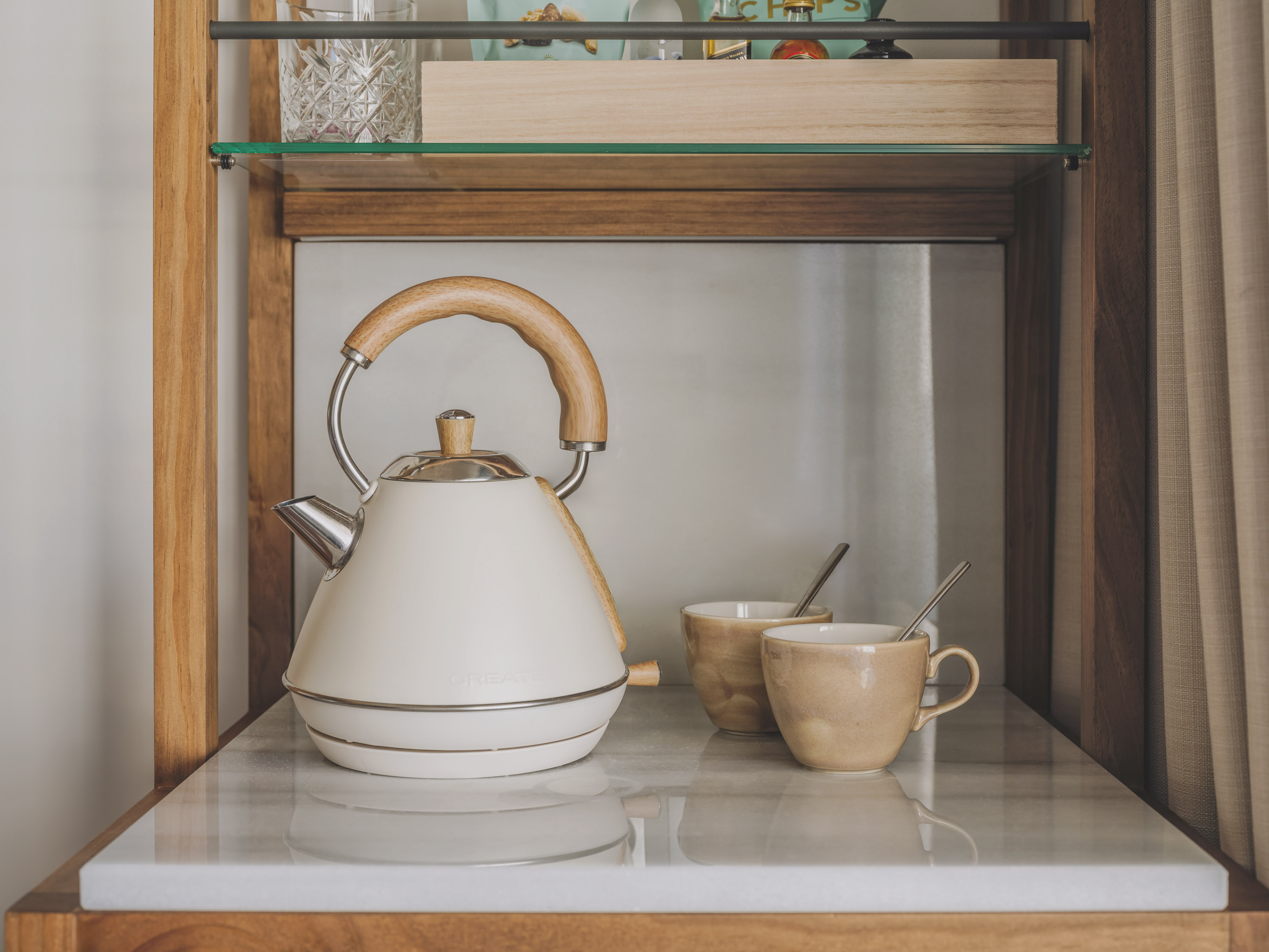 Cream electric kettle, wooden handle, and two mugs on a marble counter.