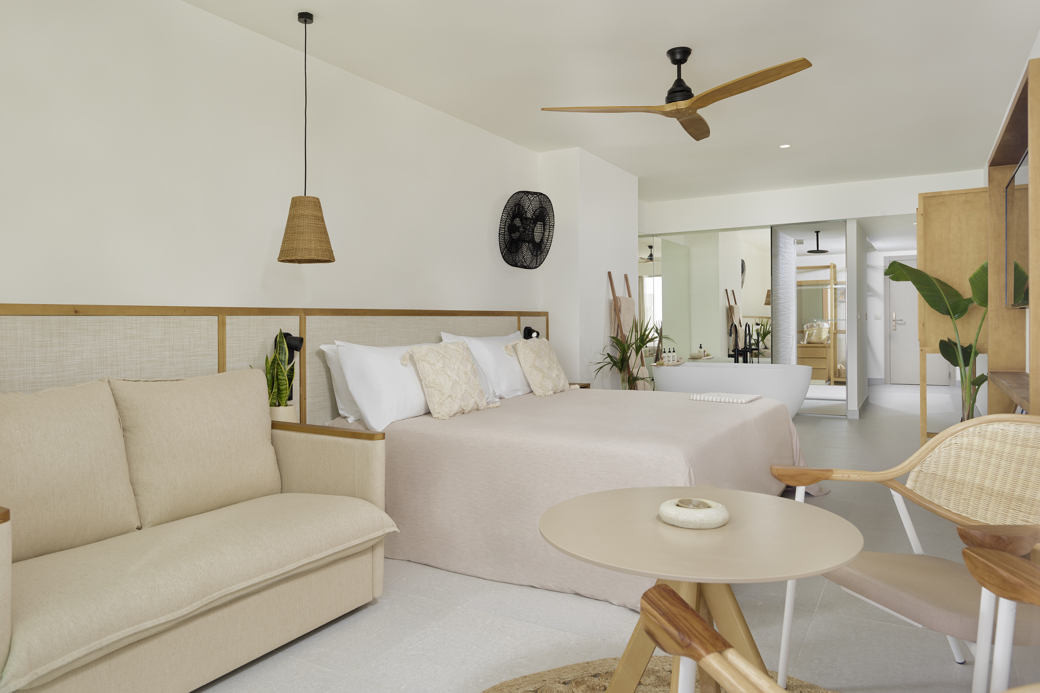 Airy bedroom suite with king bed, sofa, natural decor, and open plan bathroom.