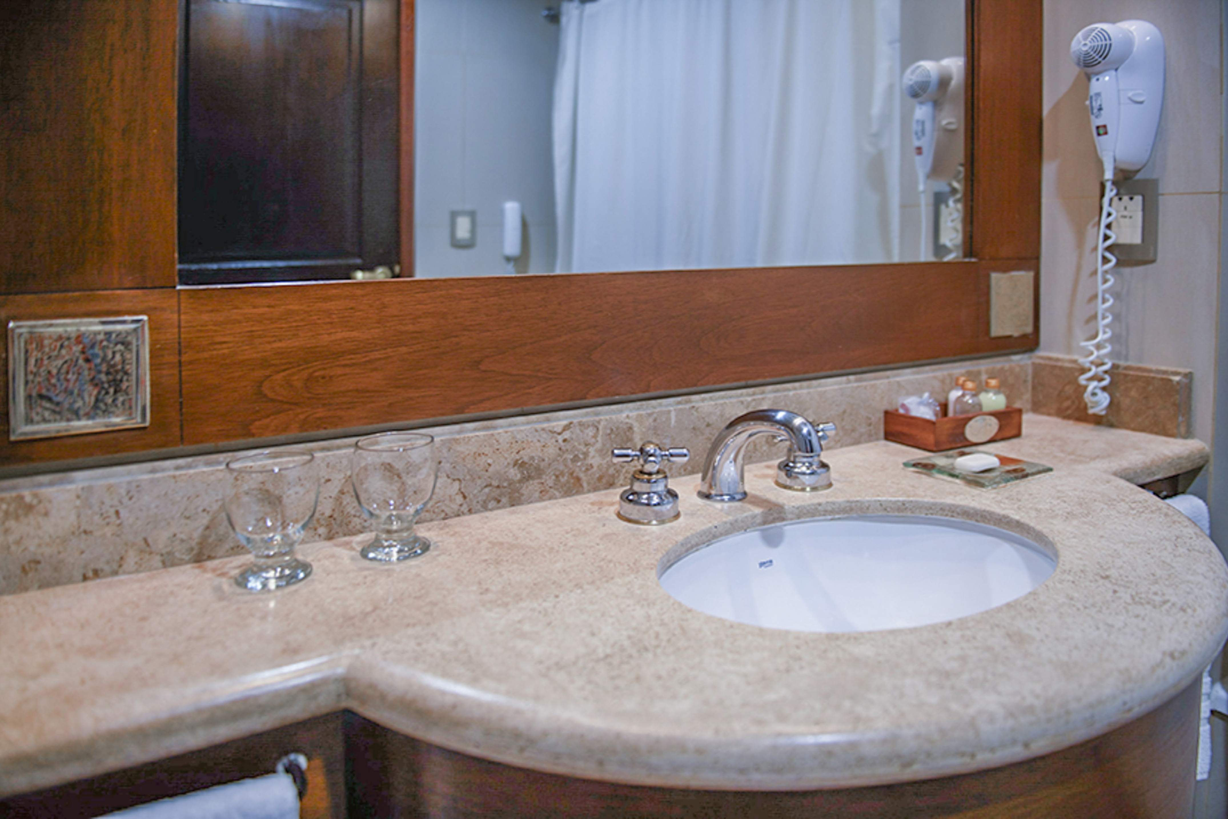 Hotel bathroom with light marble vanity, sink, mirror, and toiletries.