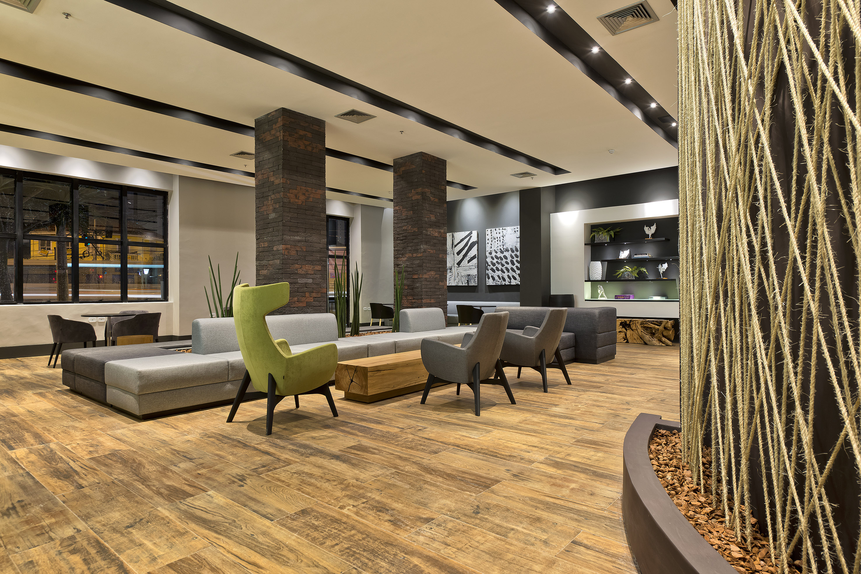 Modern hotel lobby with grey/green seating, wood floor, and brick columns.
