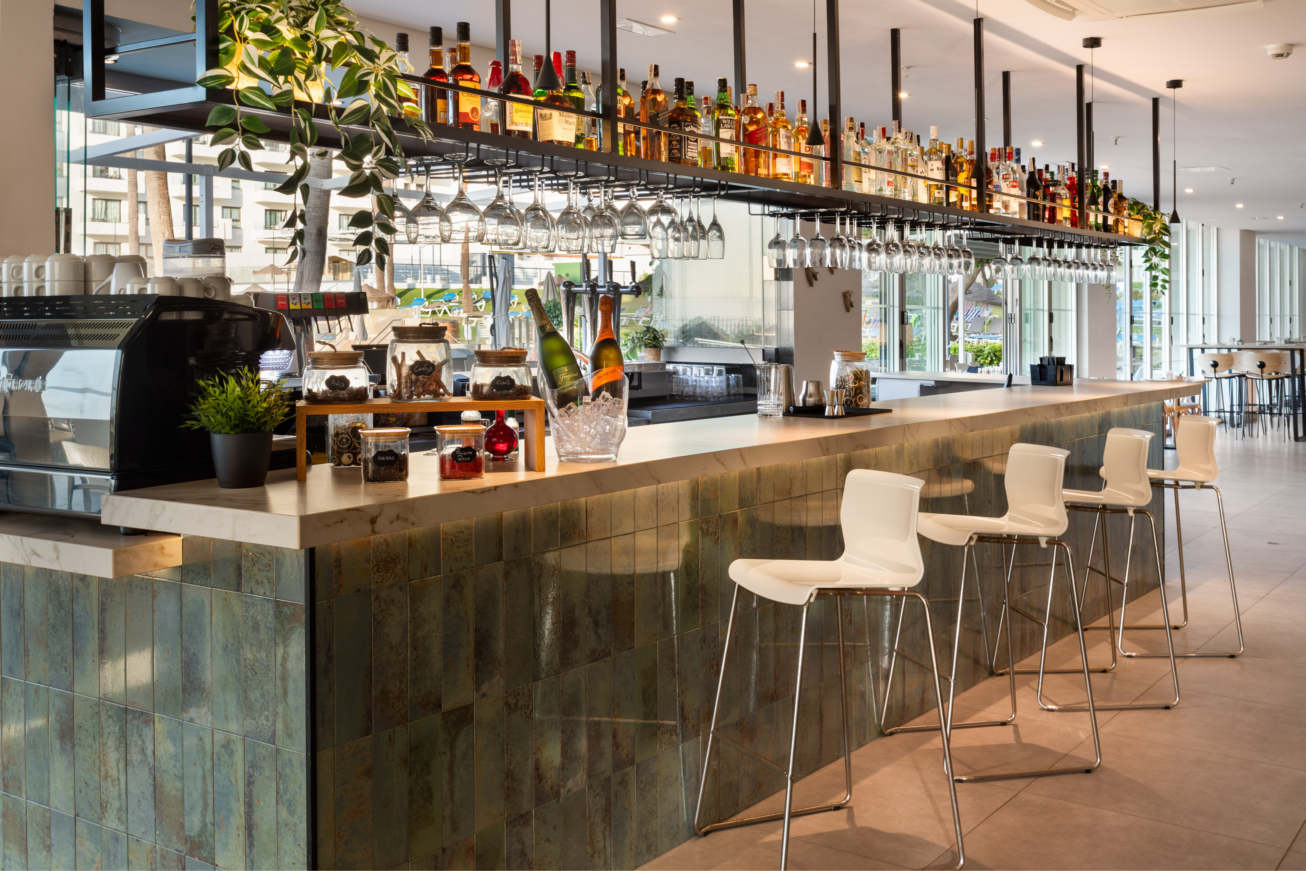 Hotel bar with liquor, hanging glasses, and sleek white stools.