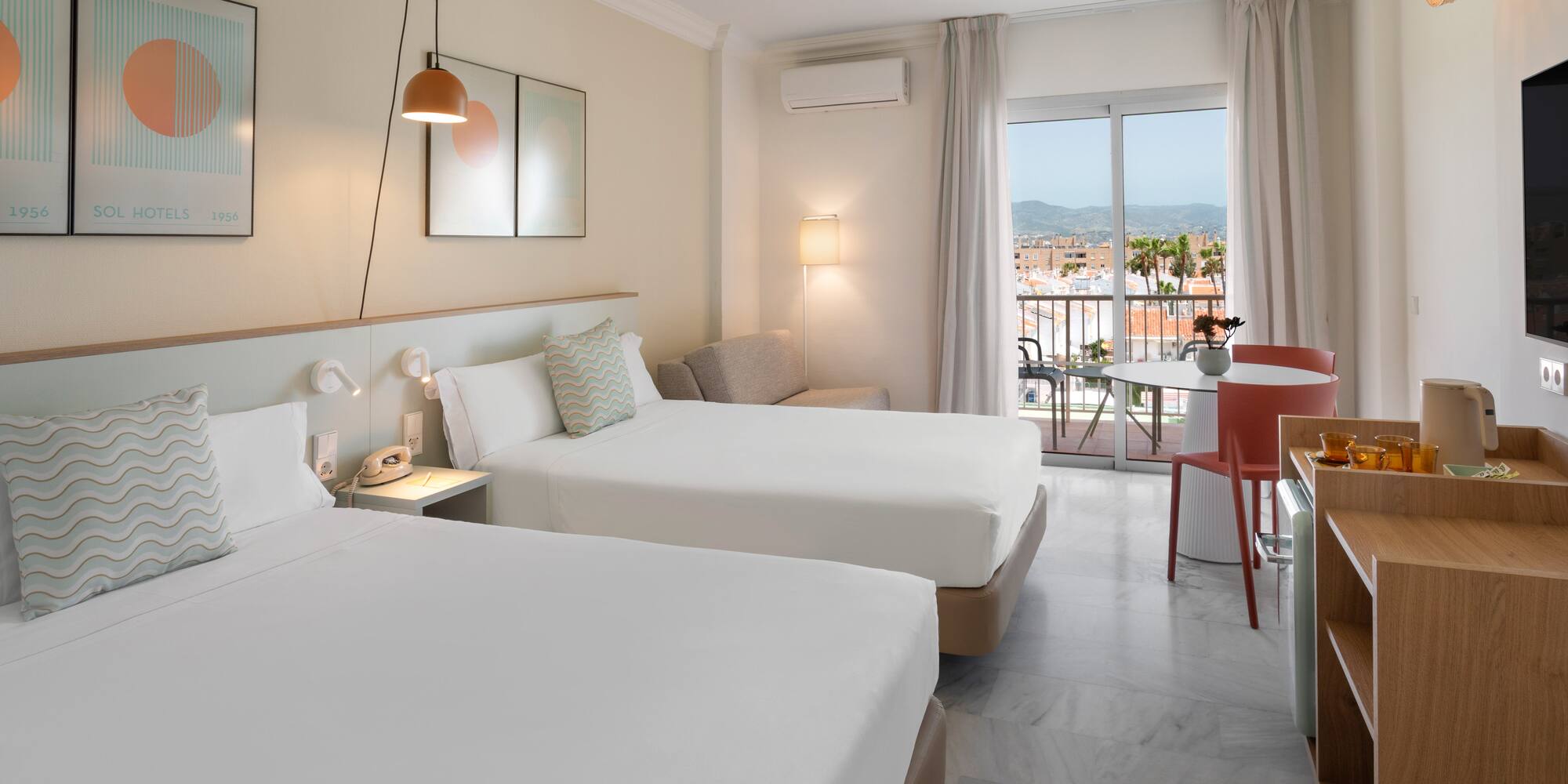 Habitación de hotel luminosa con dos camas, balcón y vistas urbanas.
