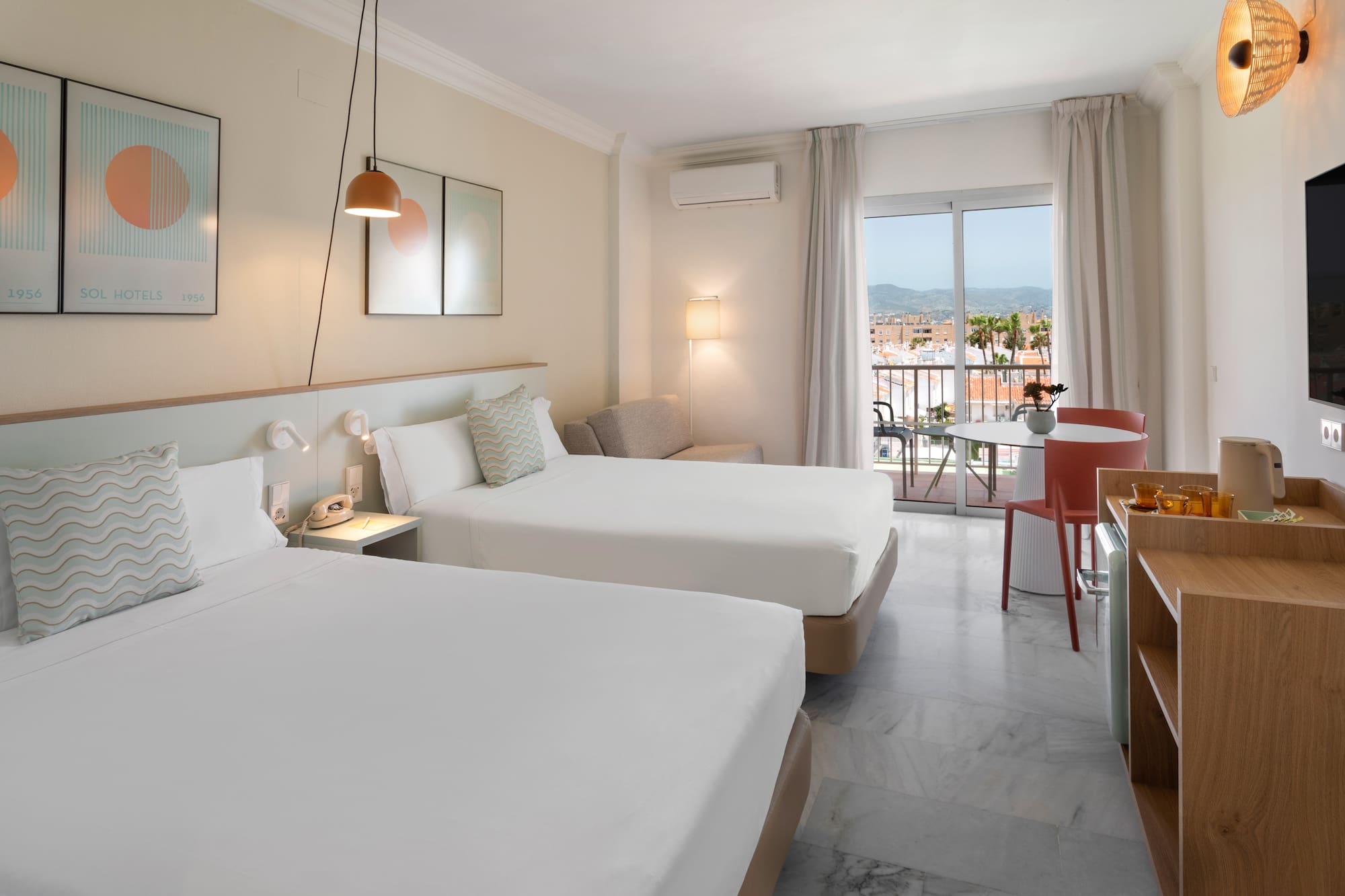 Habitación de hotel luminosa con dos camas, balcón y vistas urbanas.