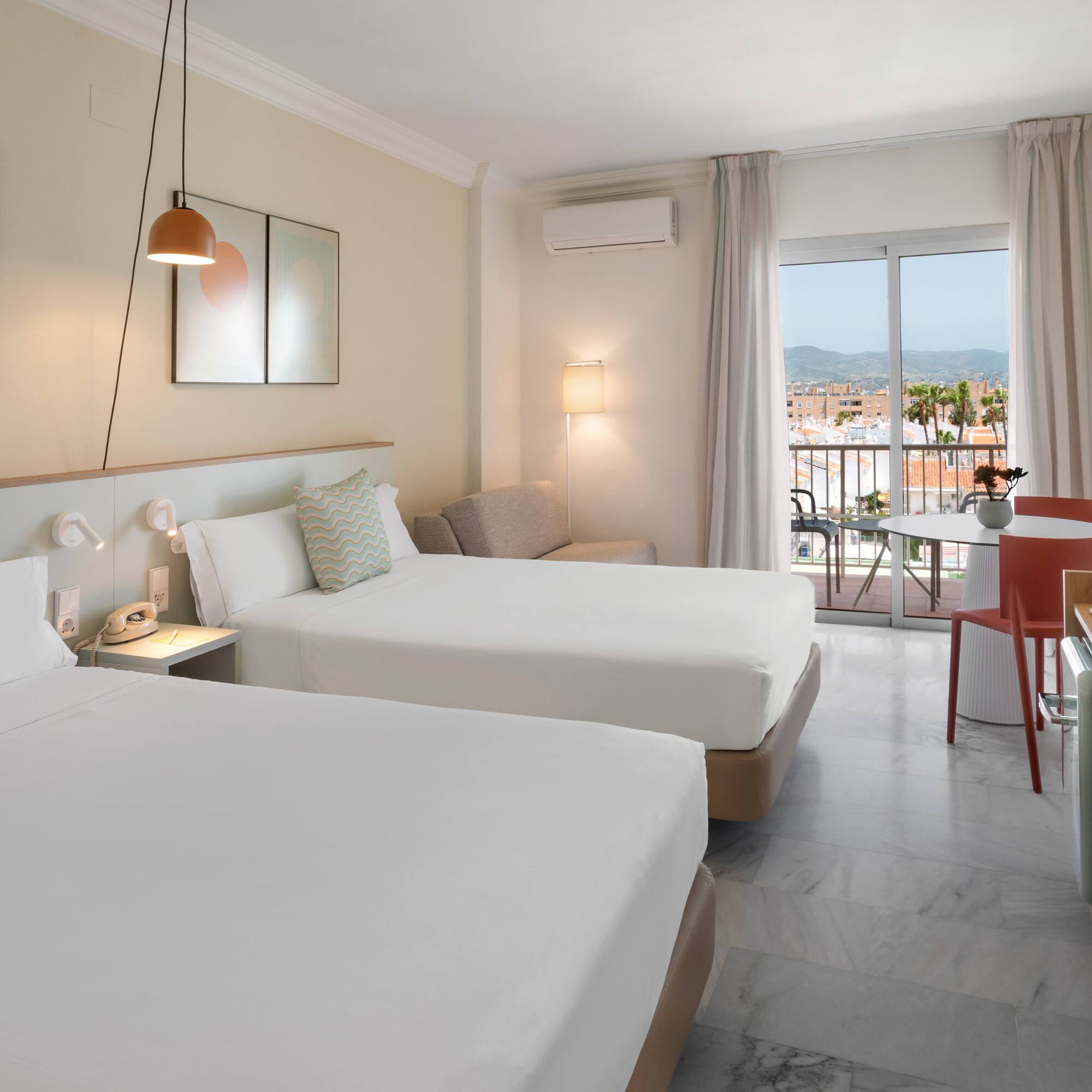 Habitación de hotel luminosa con dos camas, balcón y vistas urbanas.