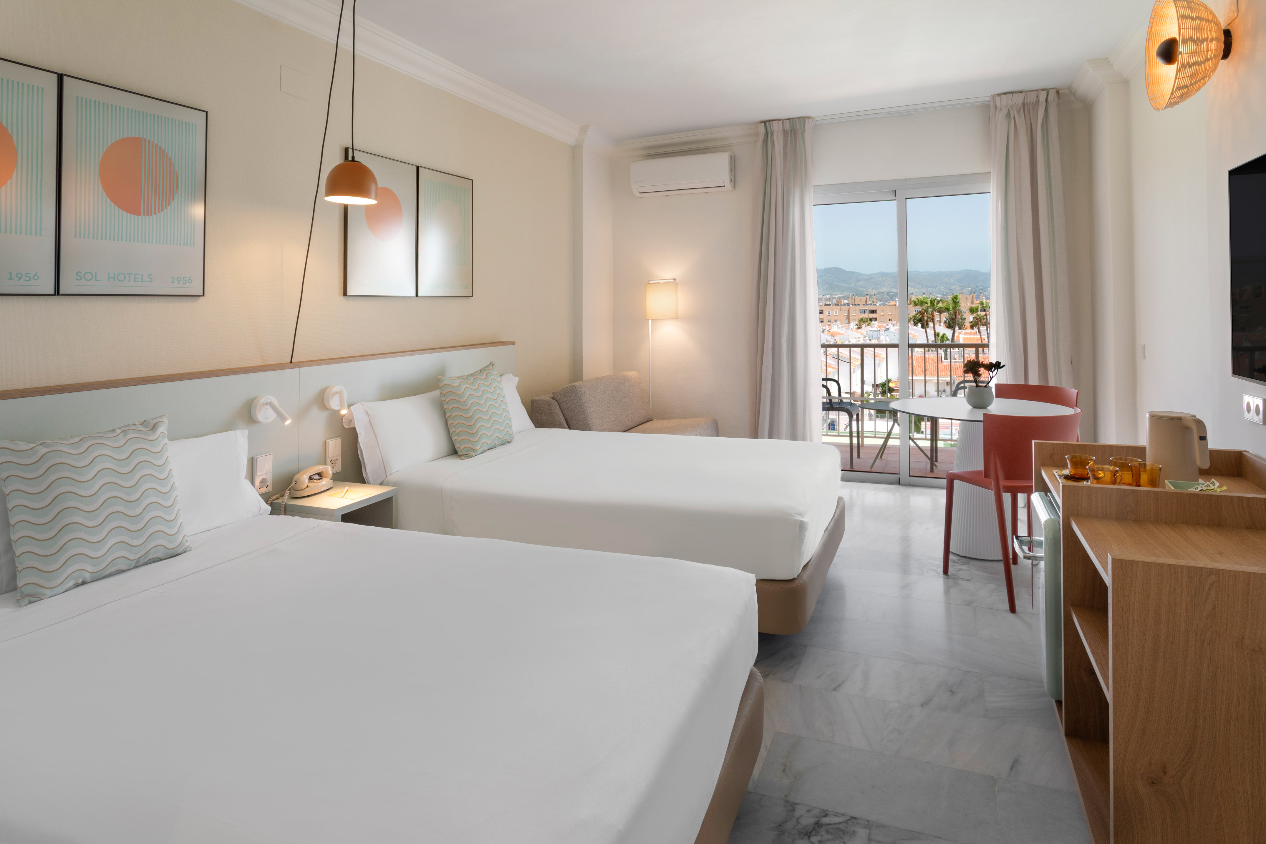 Habitación de hotel luminosa con dos camas, balcón y vistas urbanas.