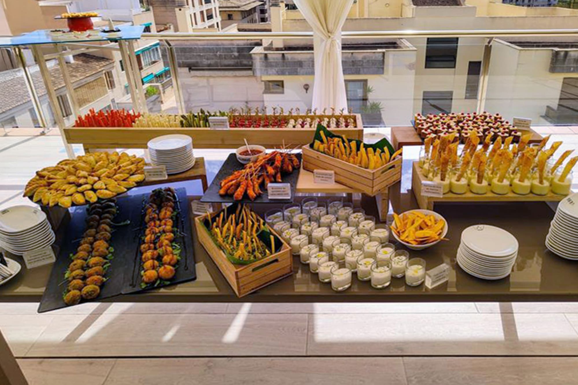 Diverse appetizer buffet with tapas, skewers, and pastries on a hotel terrace.