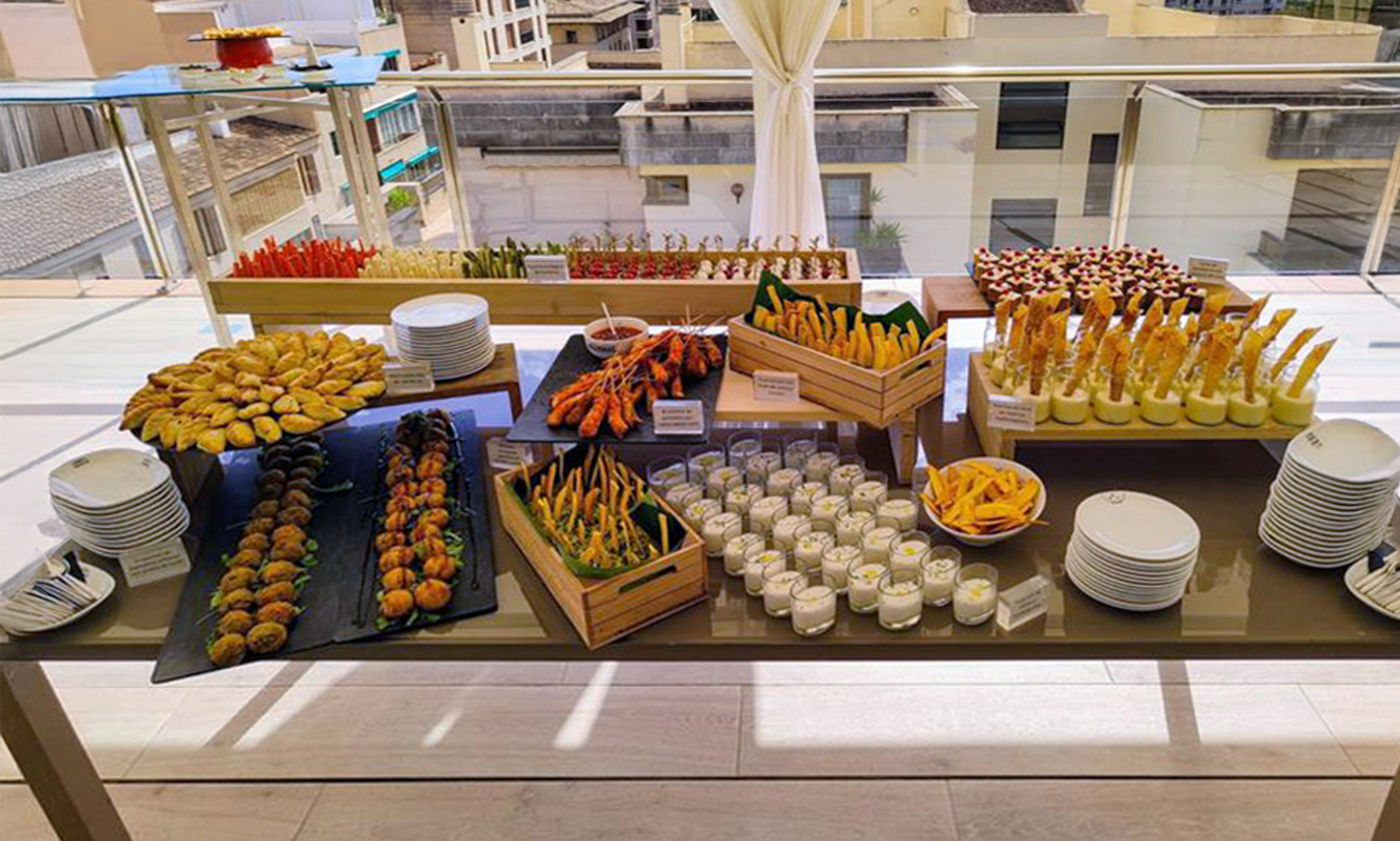 Diverse appetizer buffet with tapas, skewers, and pastries on a hotel terrace.