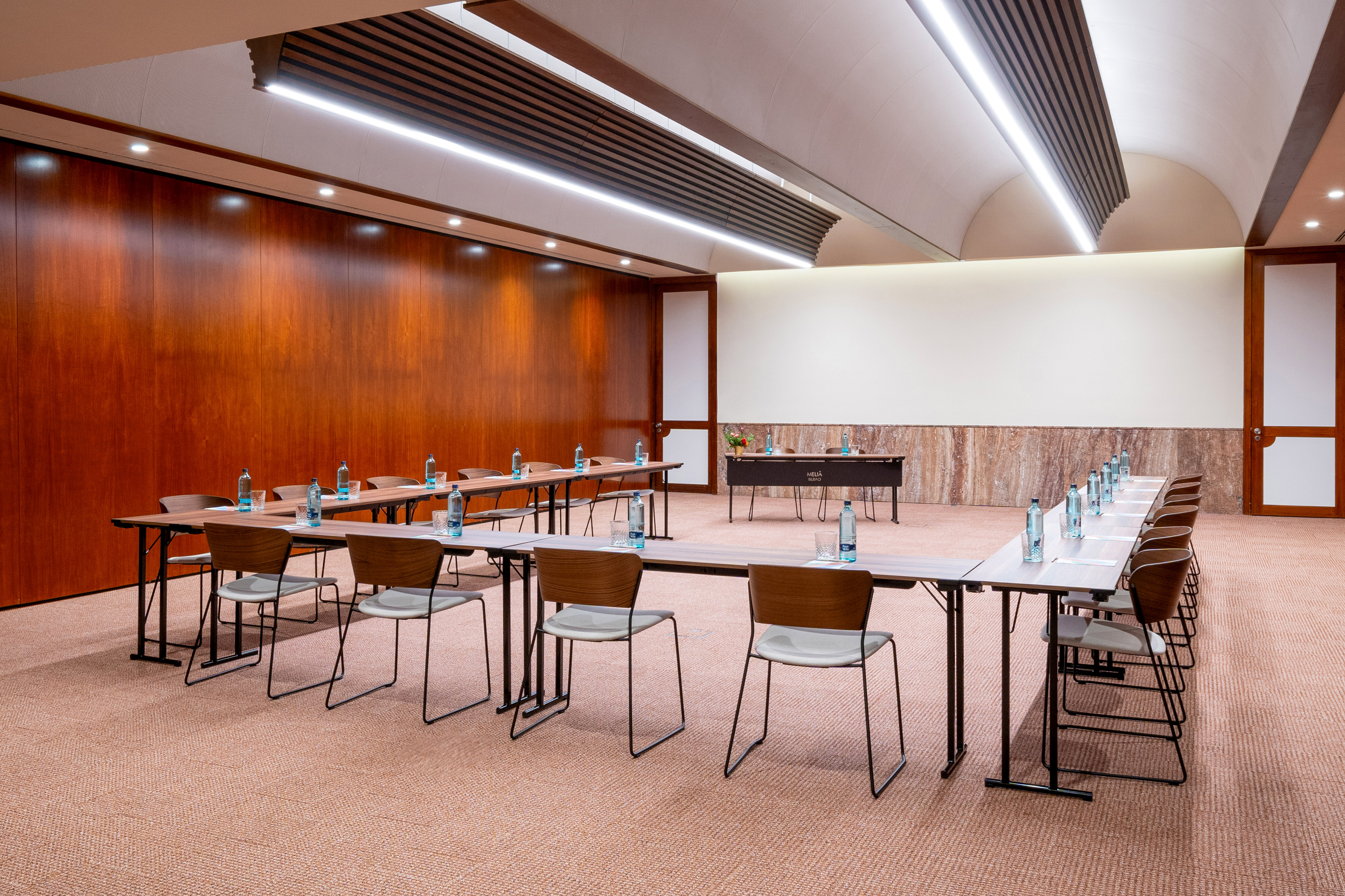 Modern hotel meeting room, U-shaped setup, wood paneled walls.