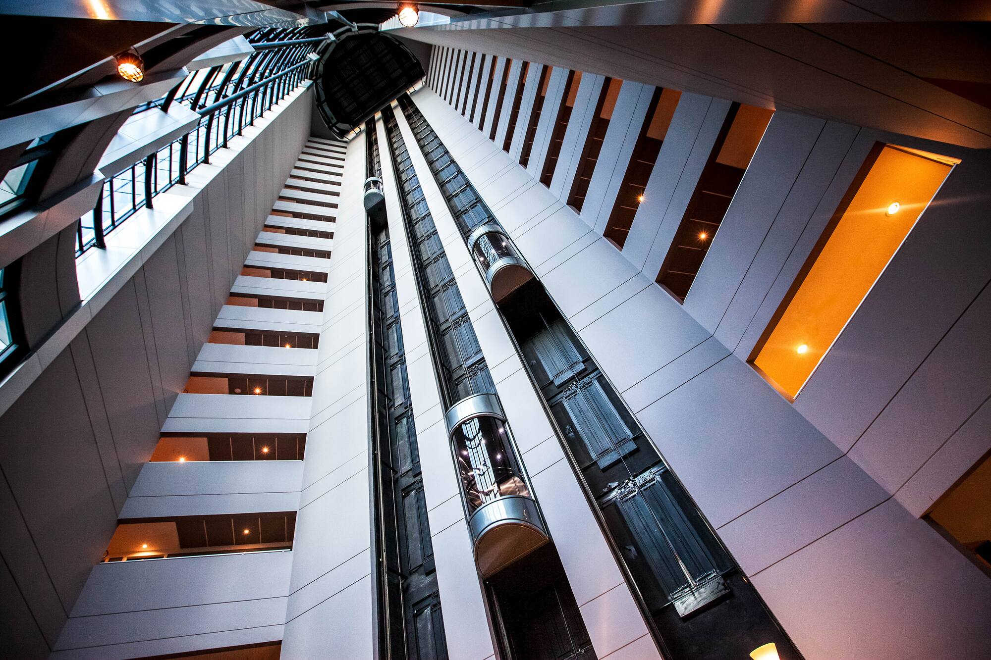 Soaring modern atrium with multiple glass elevators and warm interior lights.