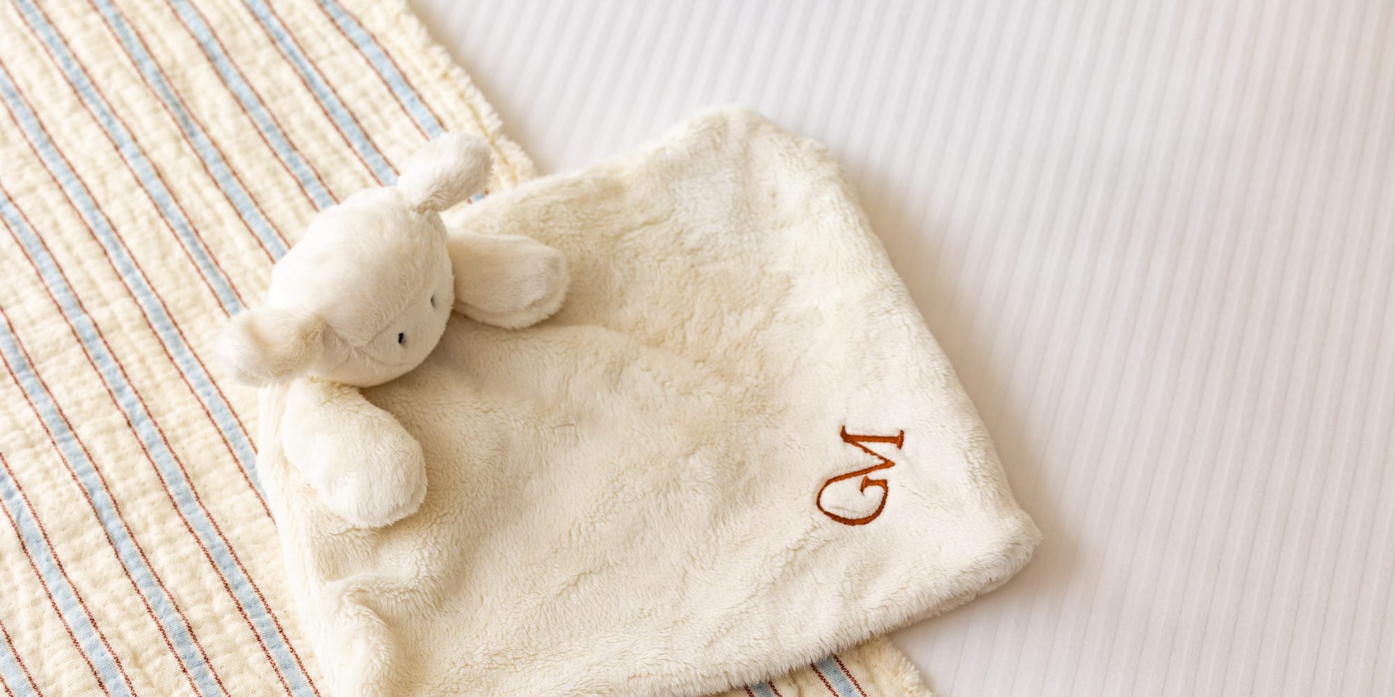 Personalized baby lamb lovey with 'GM' monogram on striped bedding.