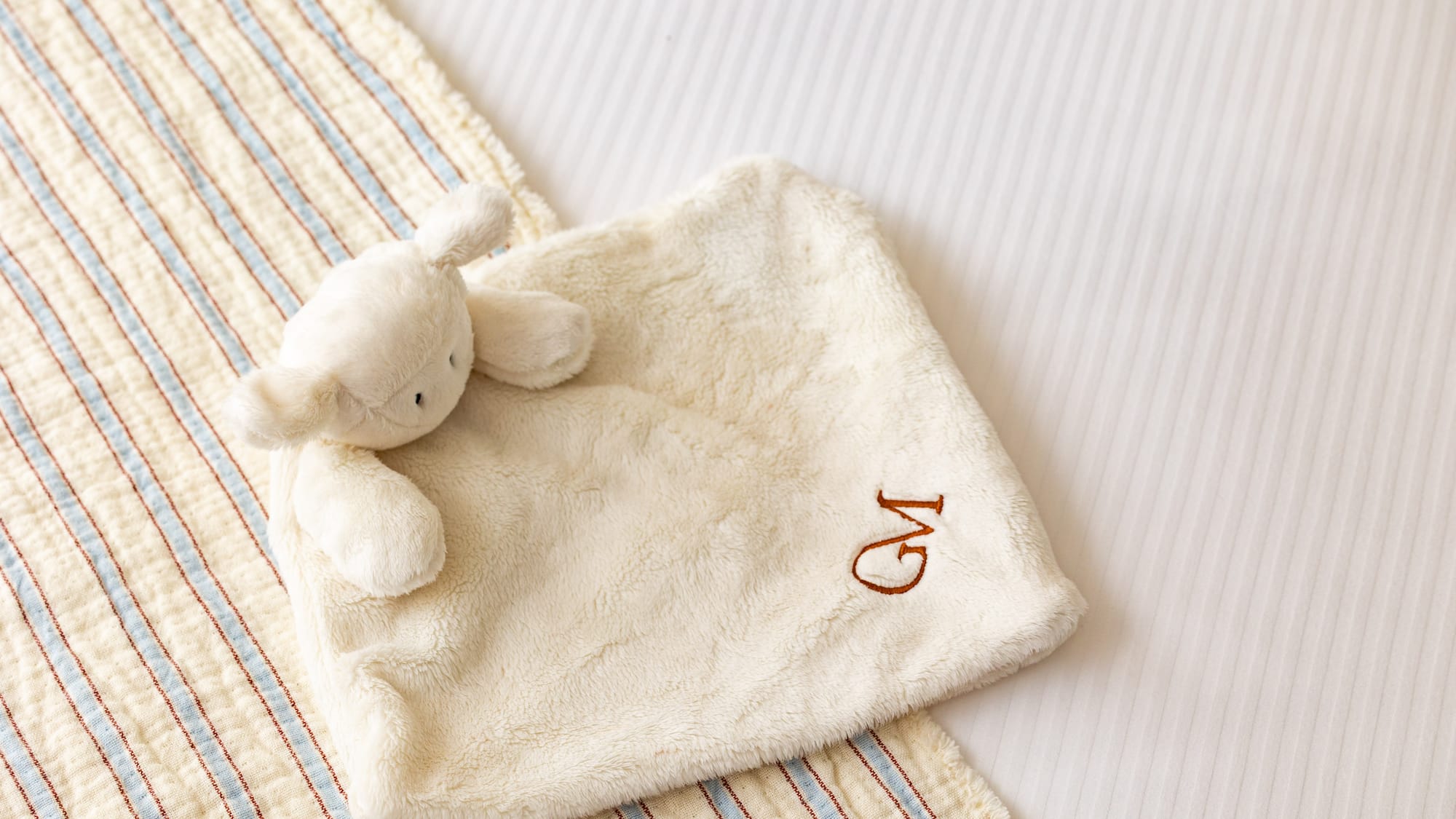Personalized baby lamb lovey with 'GM' monogram on striped bedding.
