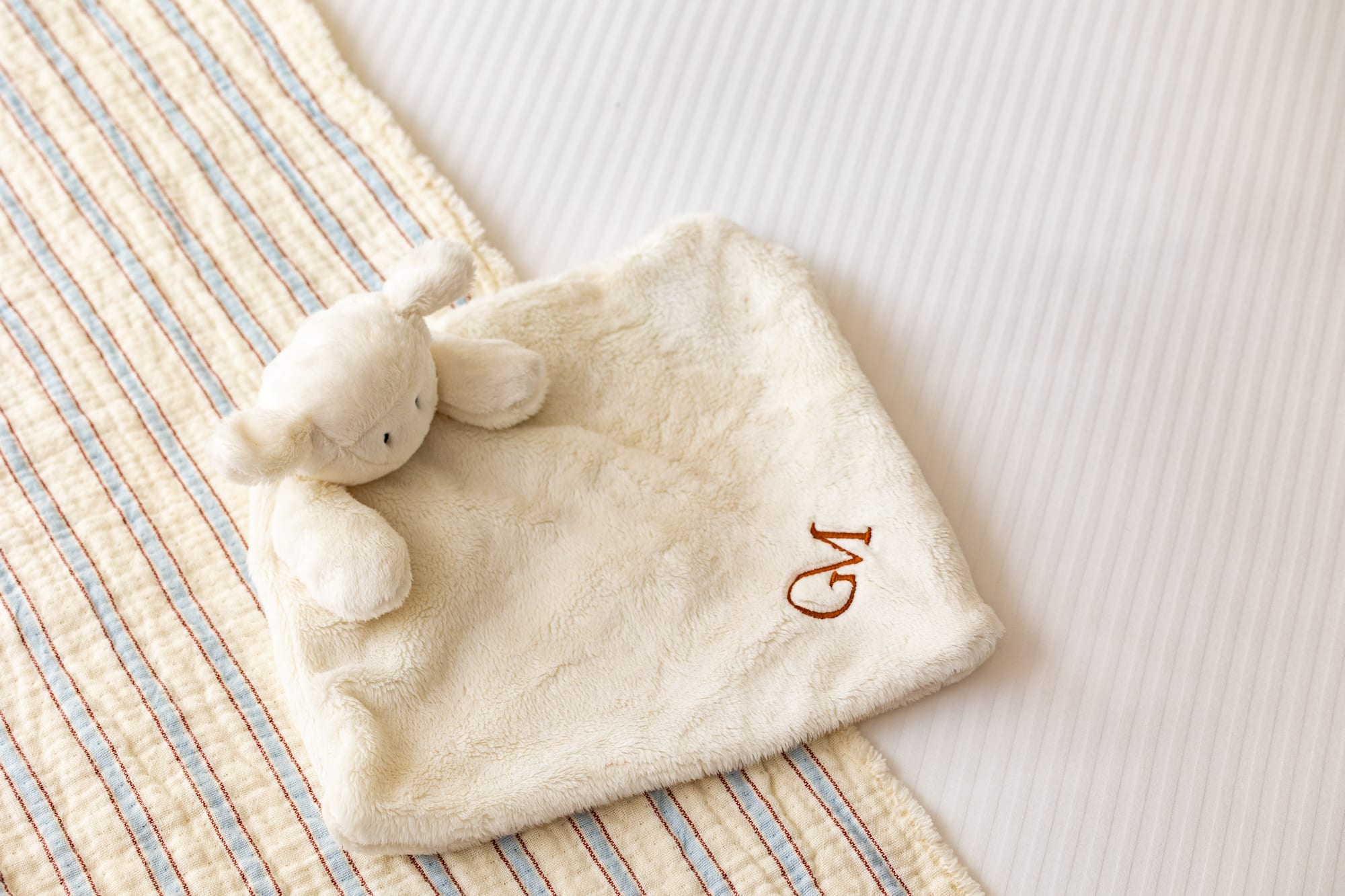 Personalized baby lamb lovey with 'GM' monogram on striped bedding.