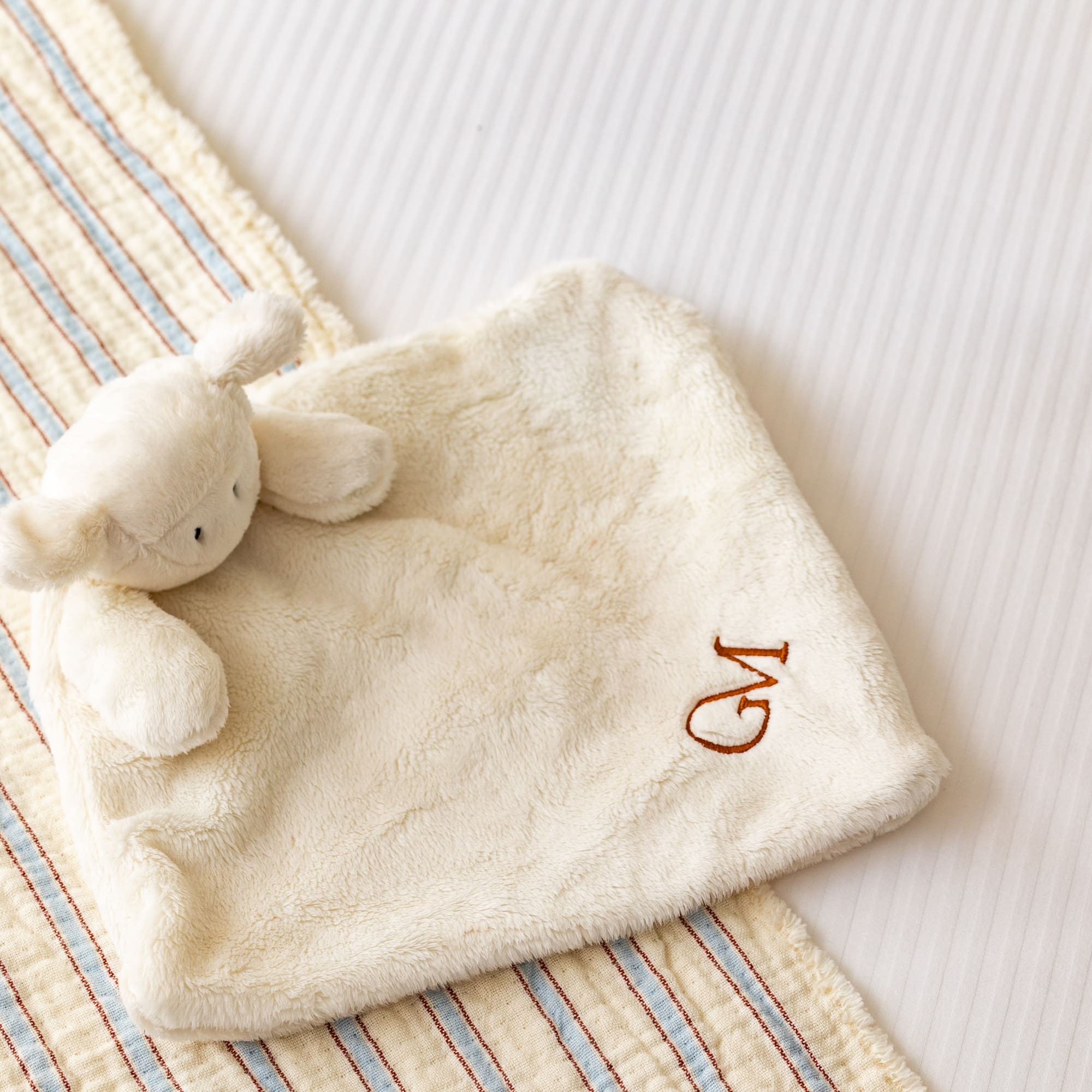 Personalized baby lamb lovey with 'GM' monogram on striped bedding.