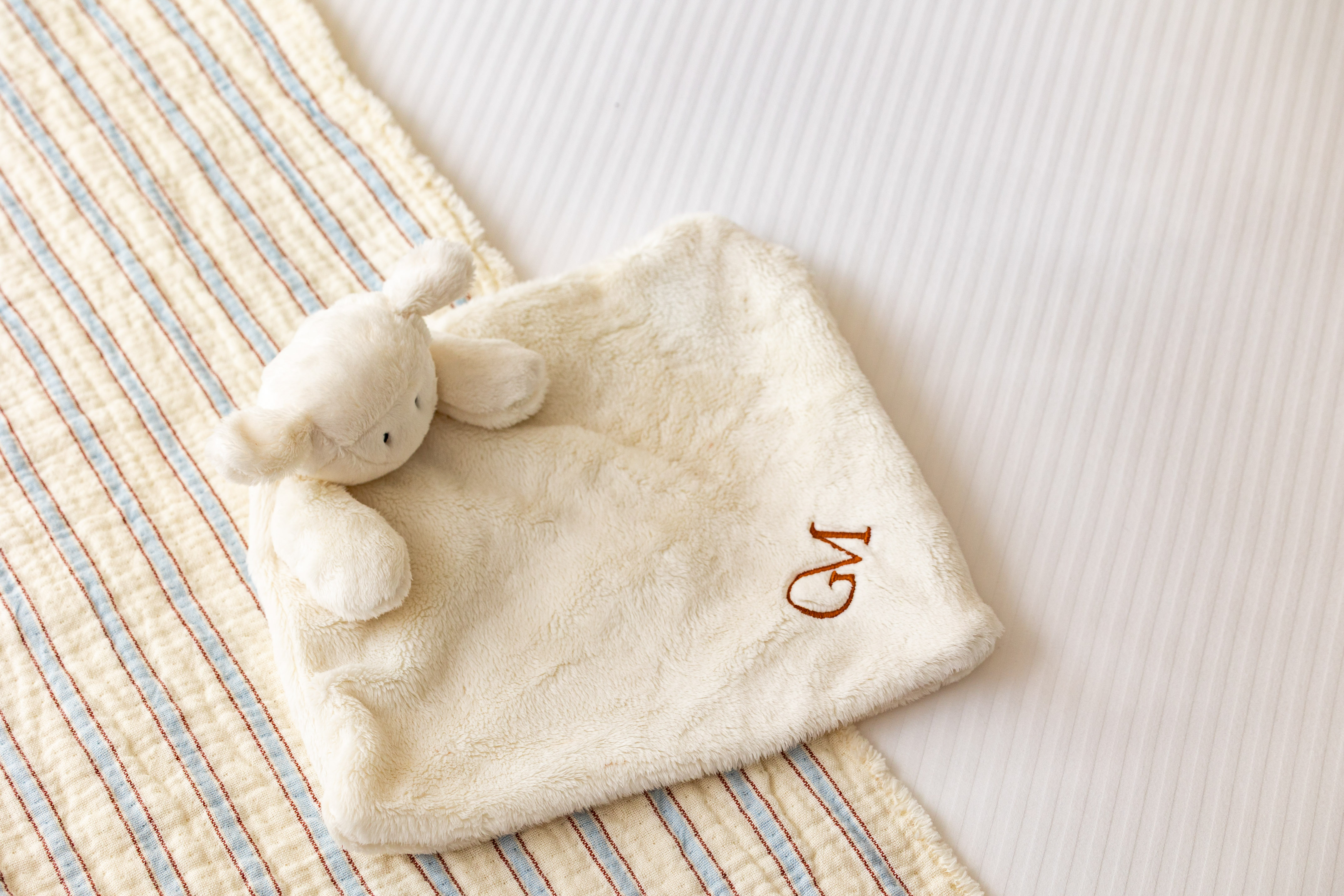 Personalized baby lamb lovey with 'GM' monogram on striped bedding.