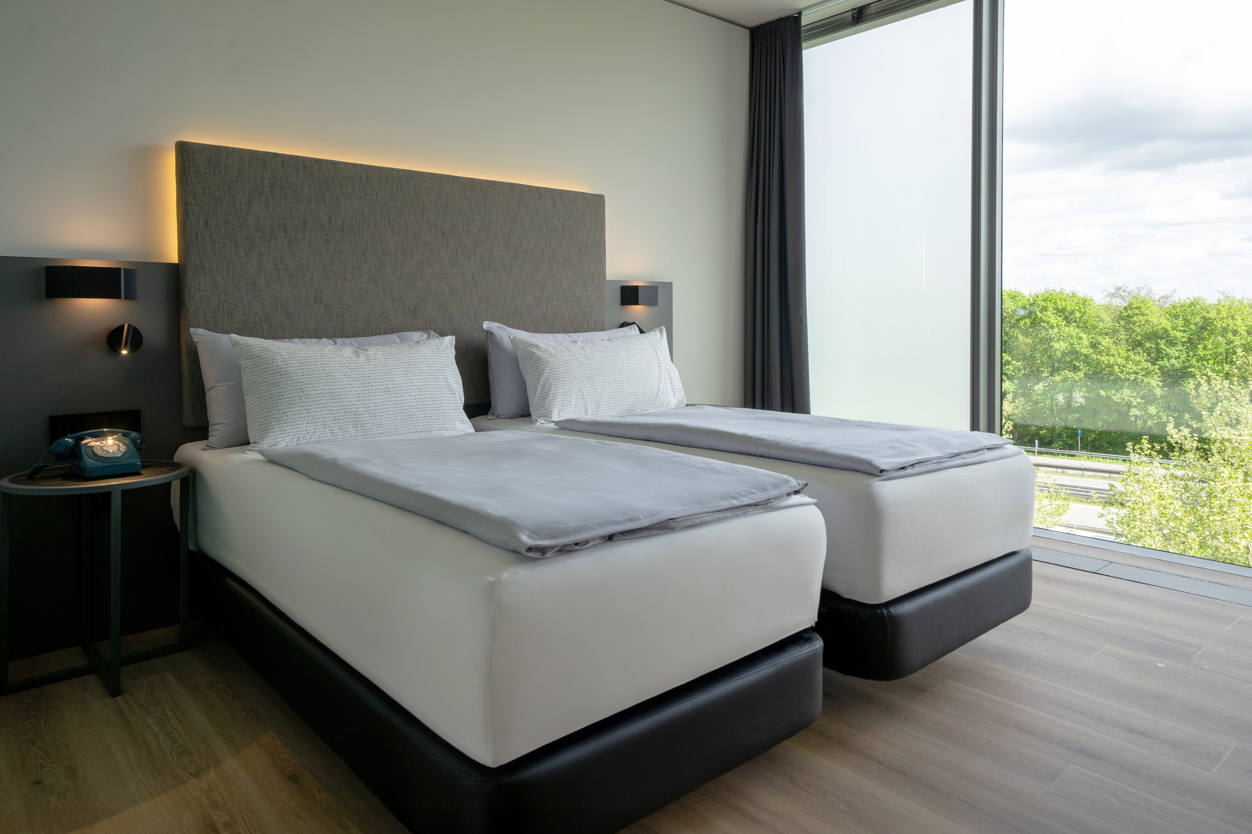 Twin beds in a modern hotel room with large window overlooking green trees.