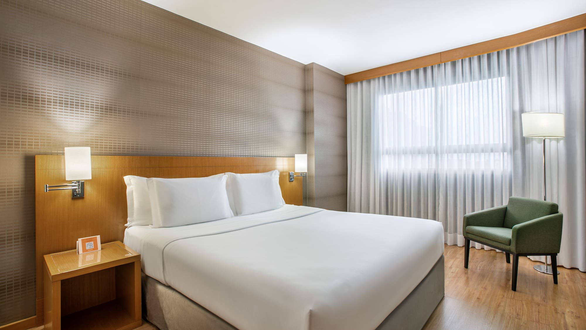 Modern hotel bedroom with king bed, green armchair, and large window.