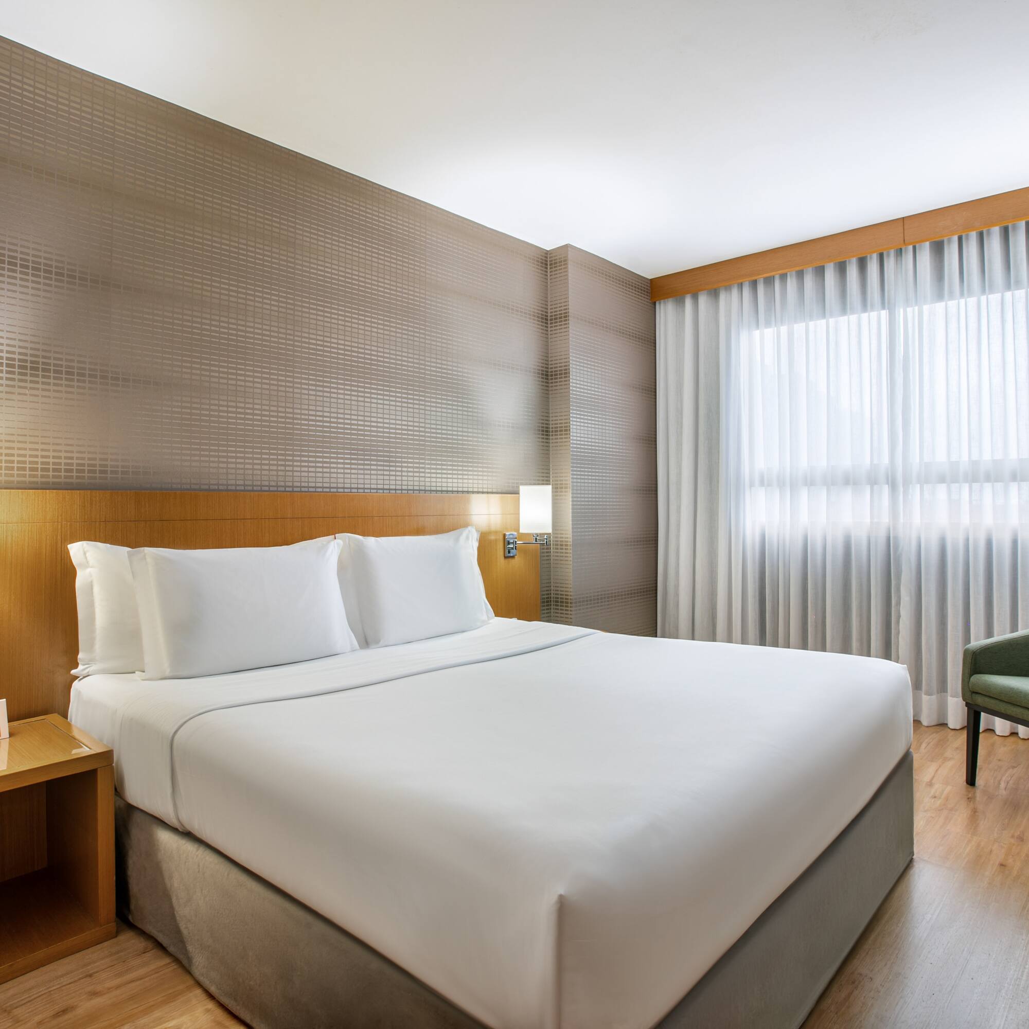 Modern hotel bedroom with king bed, green armchair, and large window.