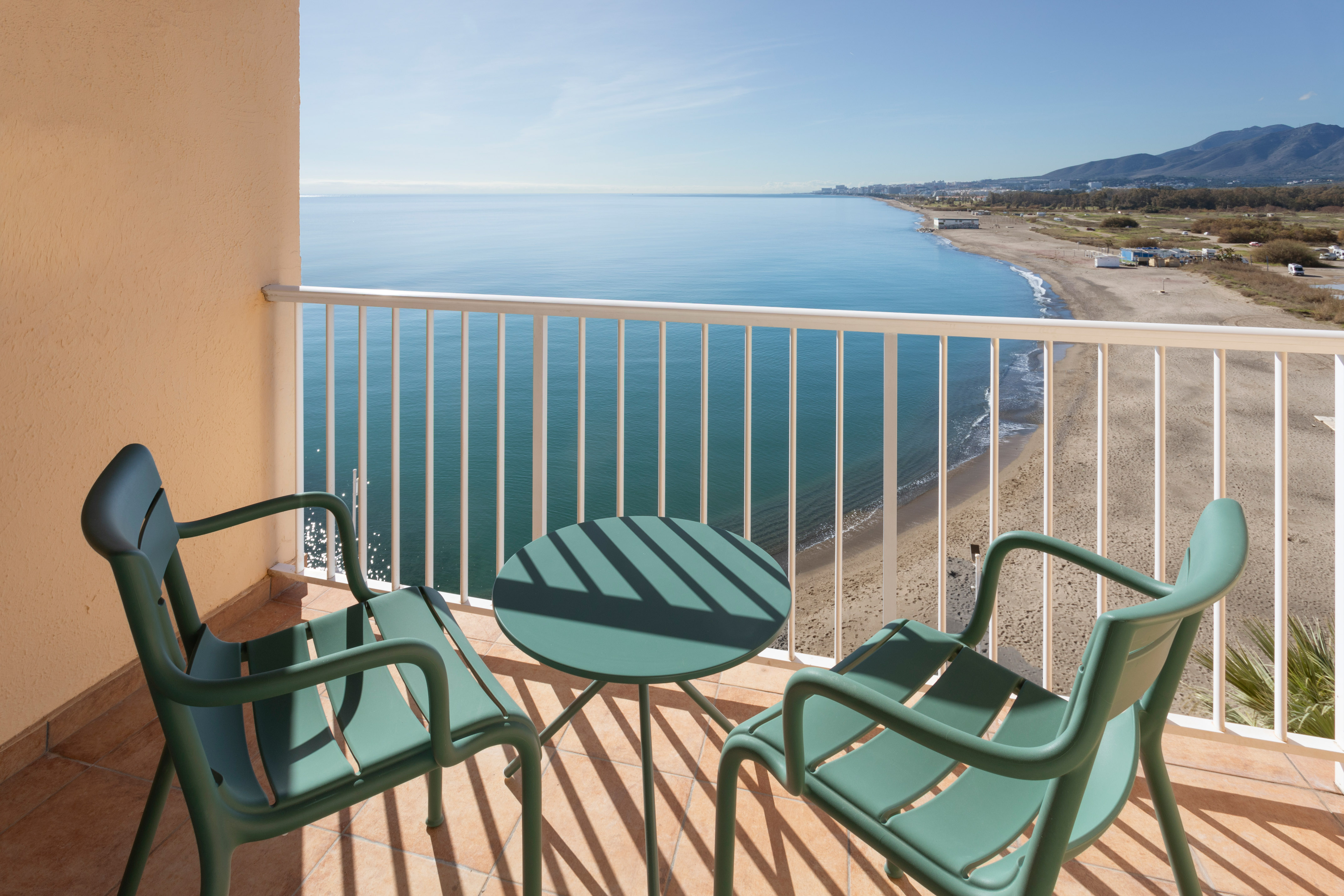 Balcón con mobiliario verde, vistas al mar Mediterráneo y playa.