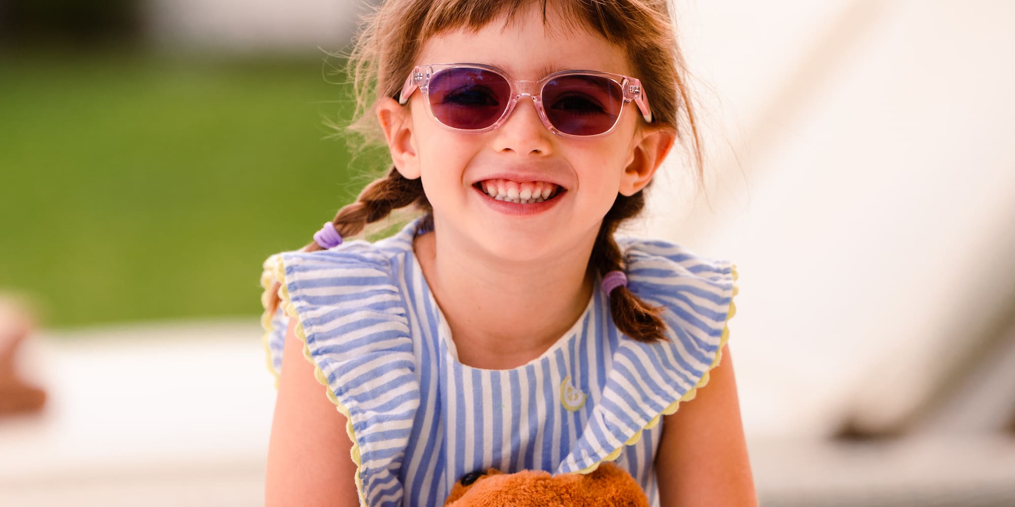 a girl wearing sunglasses and a striped dress holding a stuffed animal