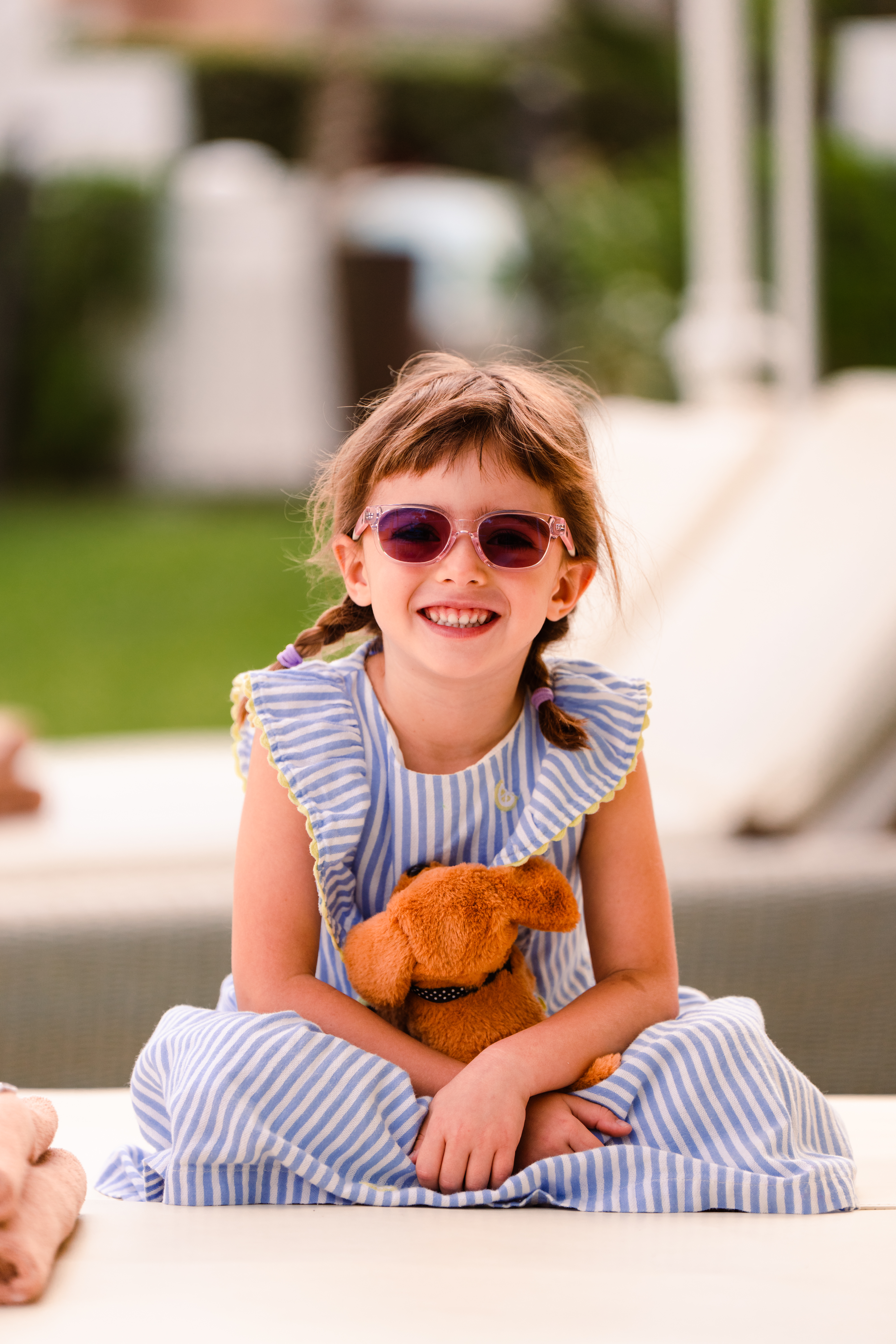 a girl wearing sunglasses and a striped dress holding a stuffed animal
