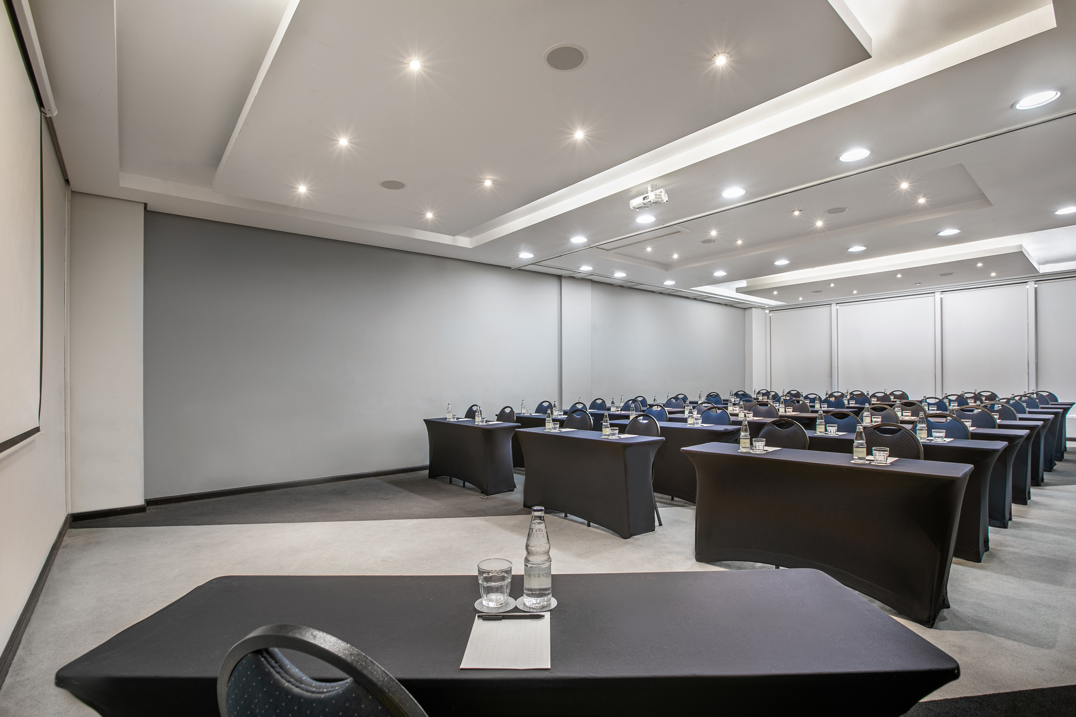 Conference room with rows of tables, chairs, water, projector, and spotlights.
