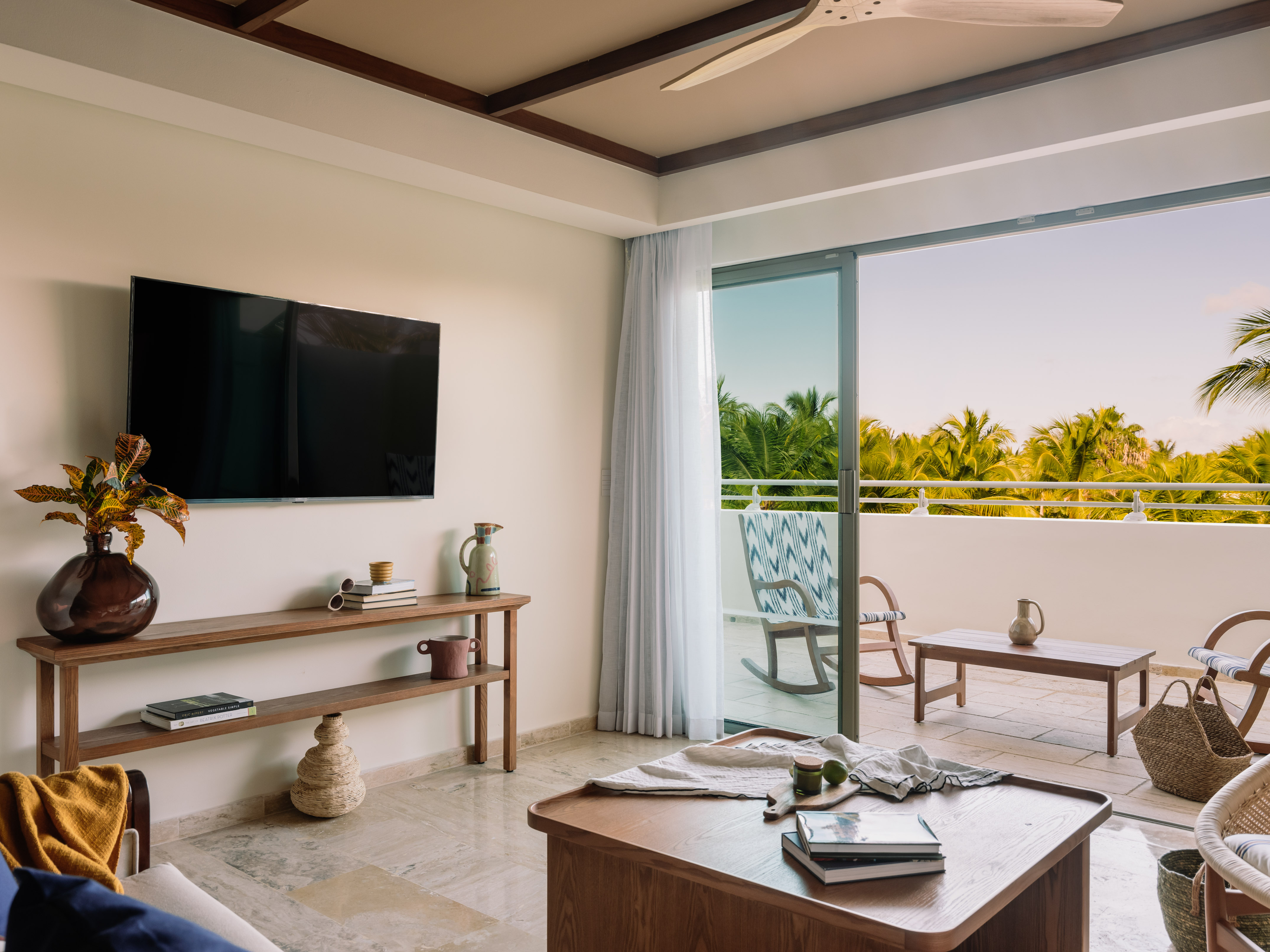 Modern living room with balcony, tropical view, TV, and wooden decor.
