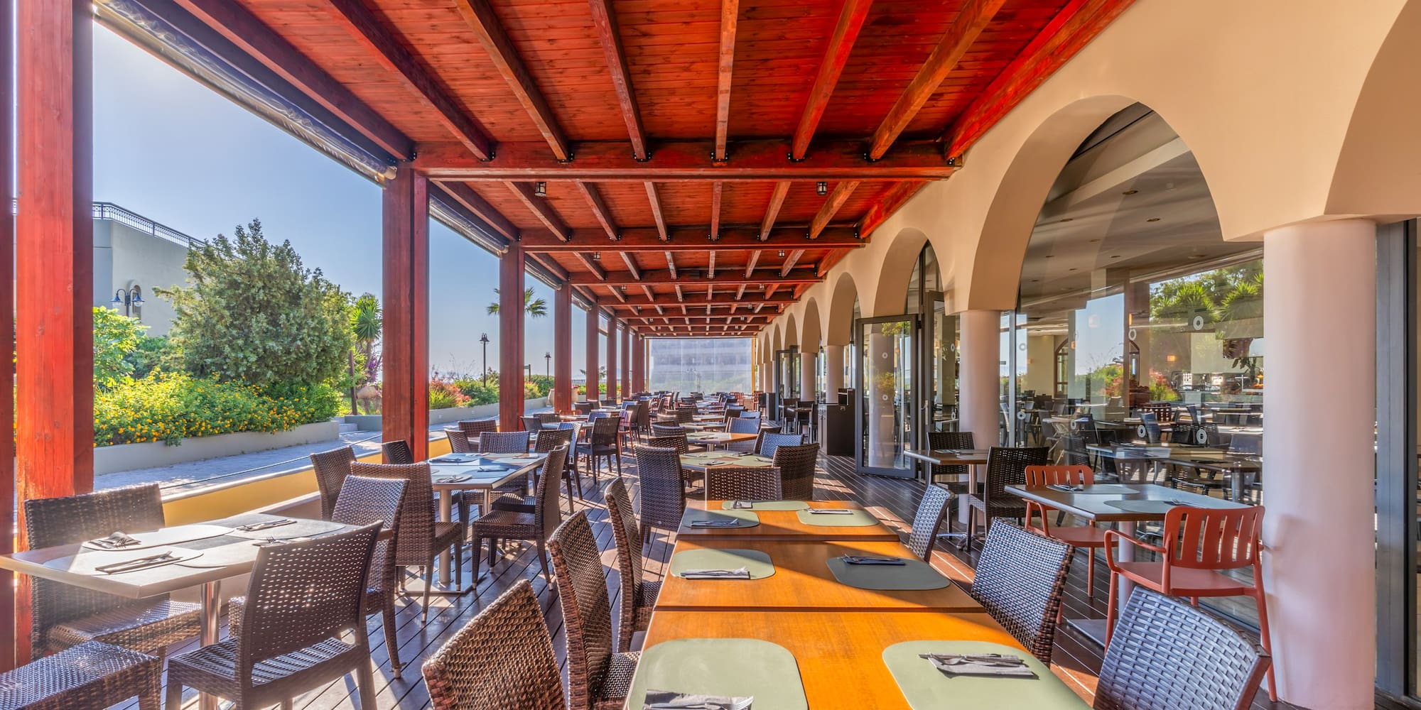 Al fresco restaurant dining under a wooden pergola with many tables.