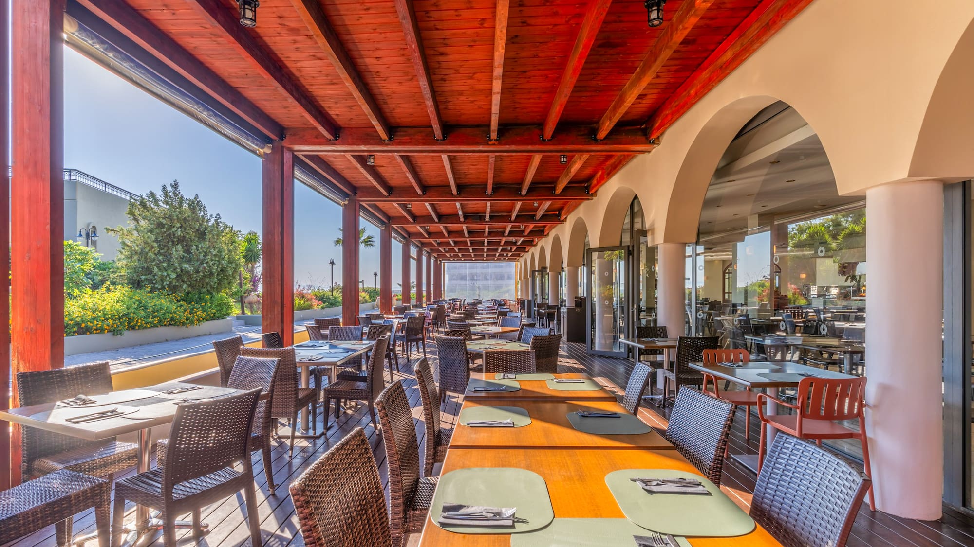 Al fresco restaurant dining under a wooden pergola with many tables.