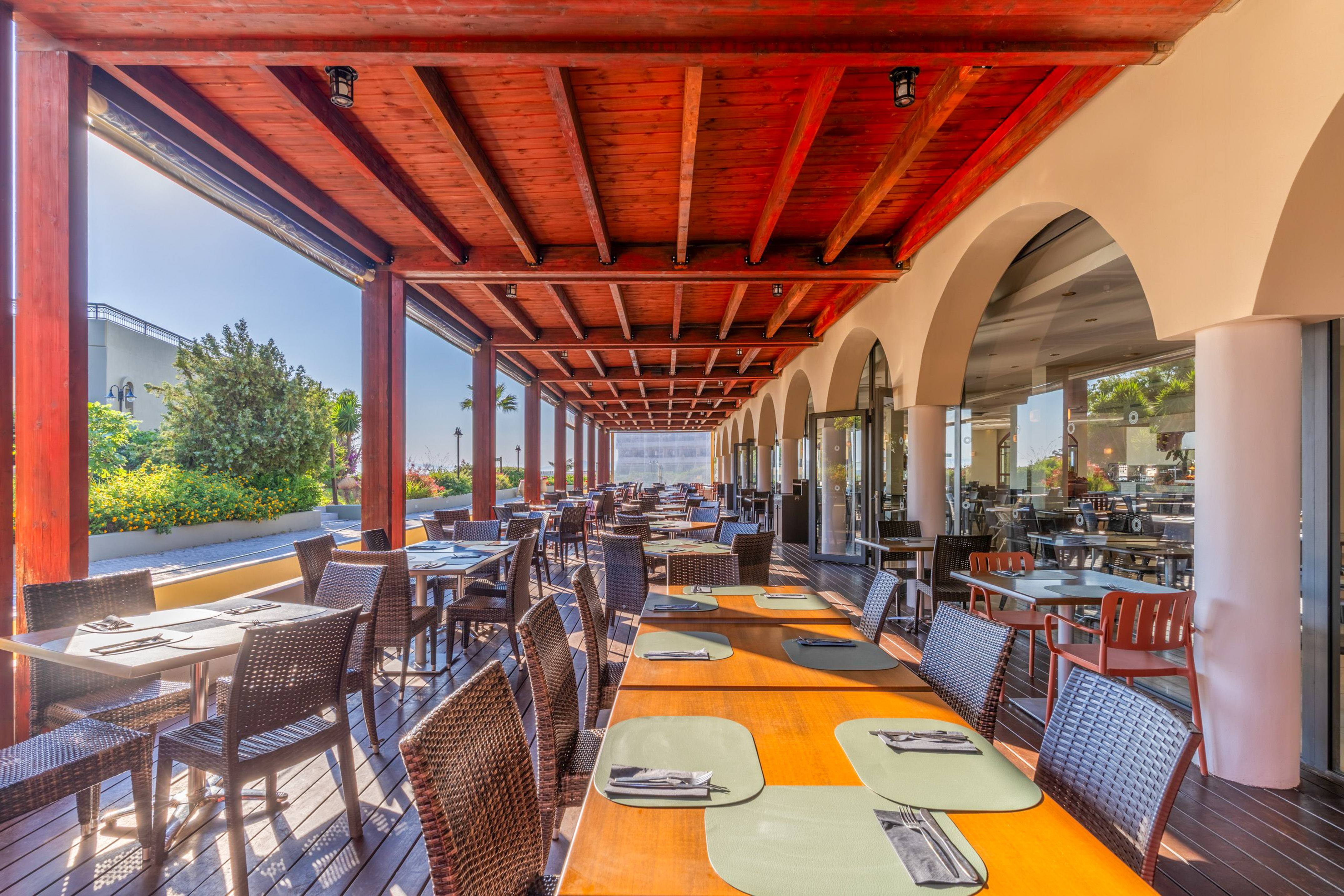 Al fresco restaurant dining under a wooden pergola with many tables.