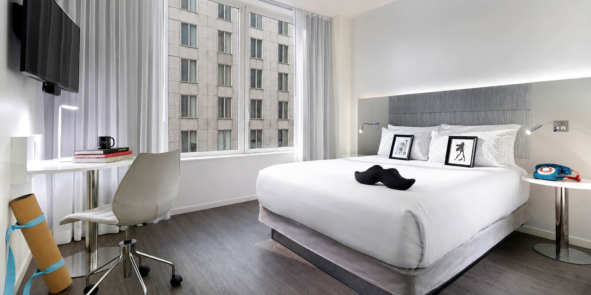 Modern hotel room with king bed, workspace, city view, and yoga mat.