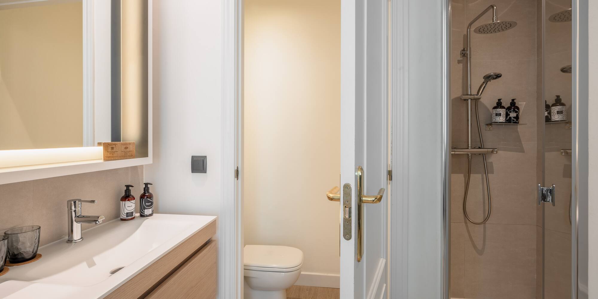 Modern bathroom with wood vanity, white sink, illuminated mirror, toilet, and shower.