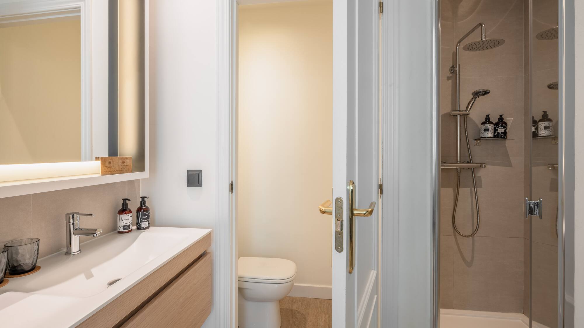 Modern bathroom with wood vanity, white sink, illuminated mirror, toilet, and shower.