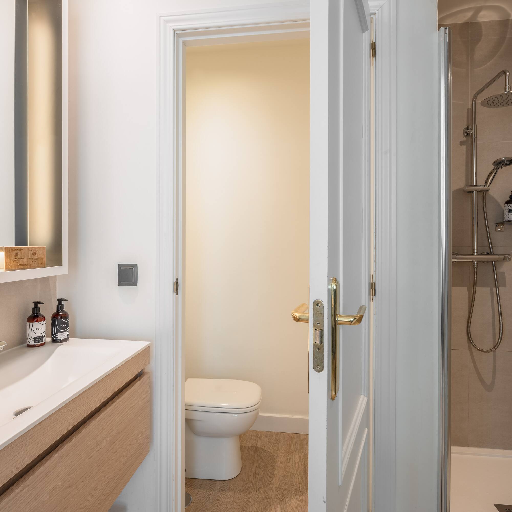 Modern bathroom with wood vanity, white sink, illuminated mirror, toilet, and shower.
