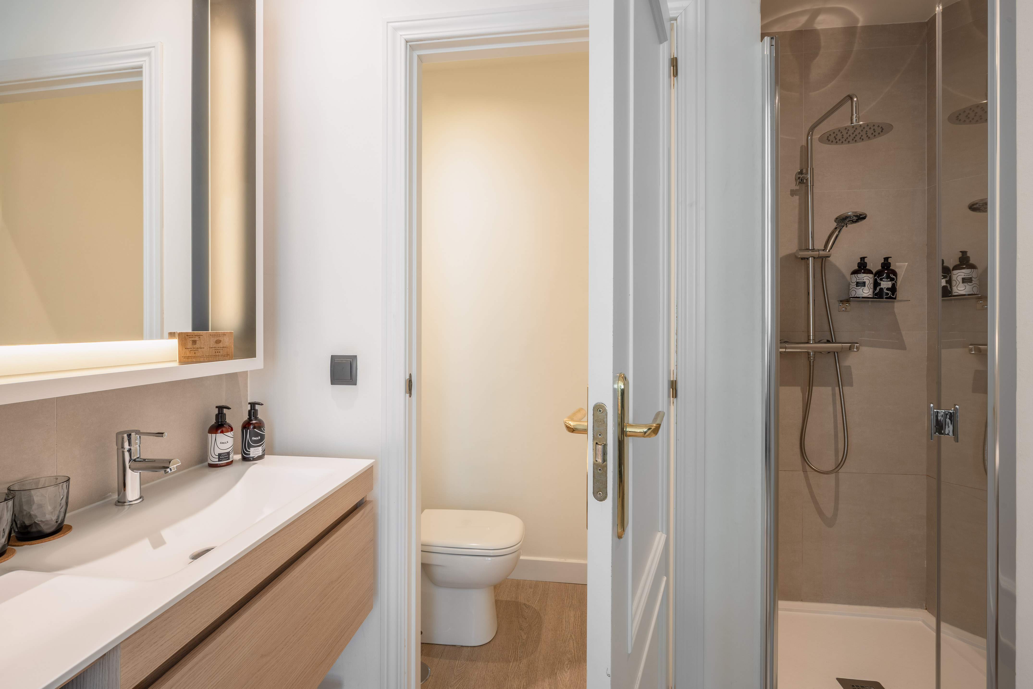 Modern bathroom with wood vanity, white sink, illuminated mirror, toilet, and shower.