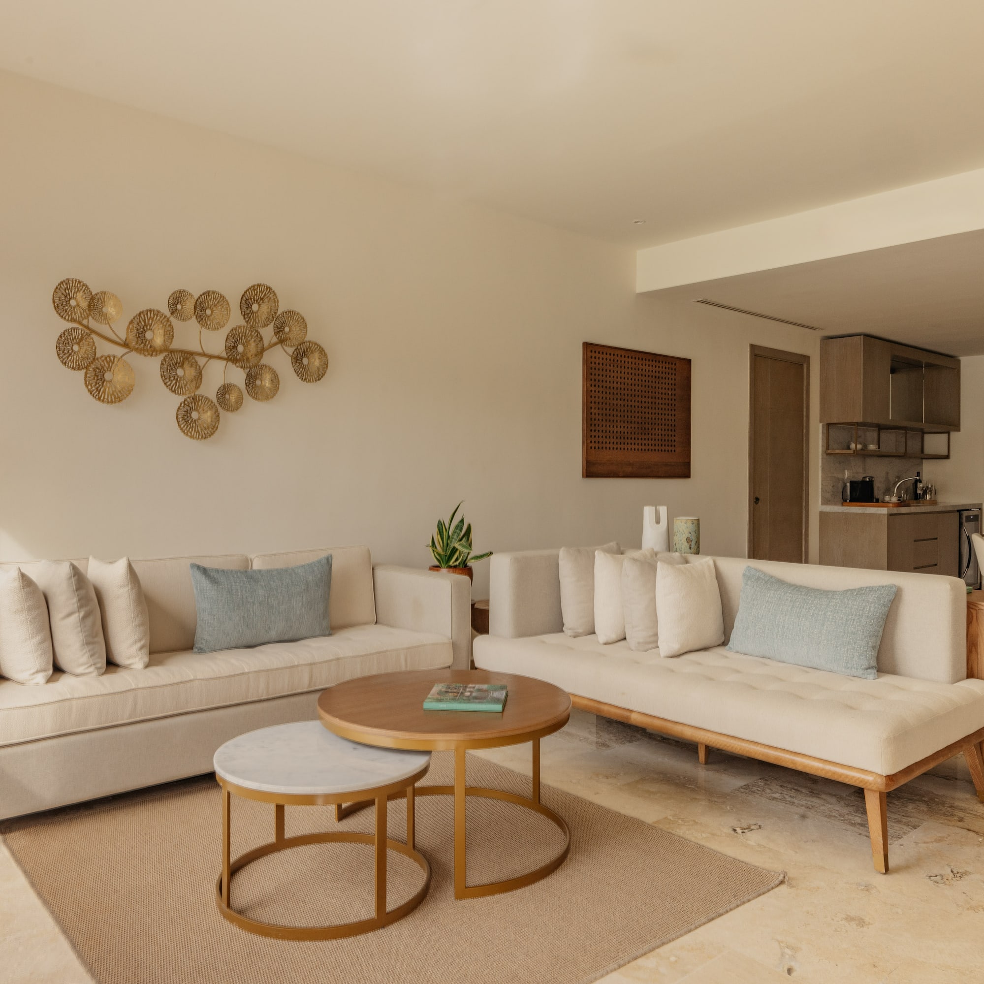 Modern living room with neutral sofas, nesting coffee tables, gold wall art.