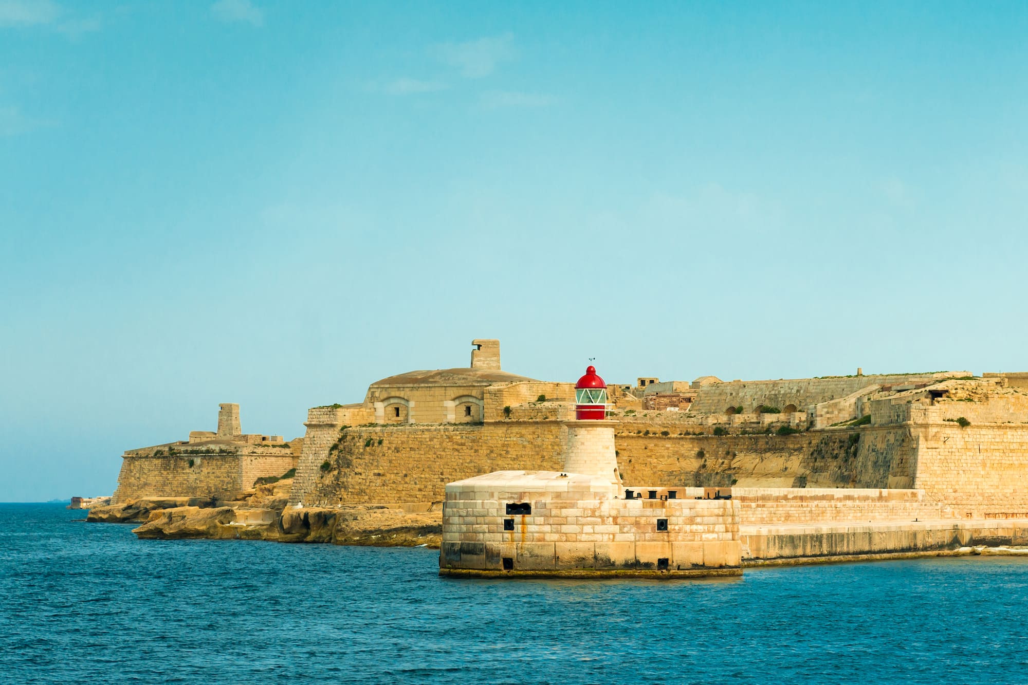 Historic fortifications and red lighthouse guarding Grand Harbour, Valletta.