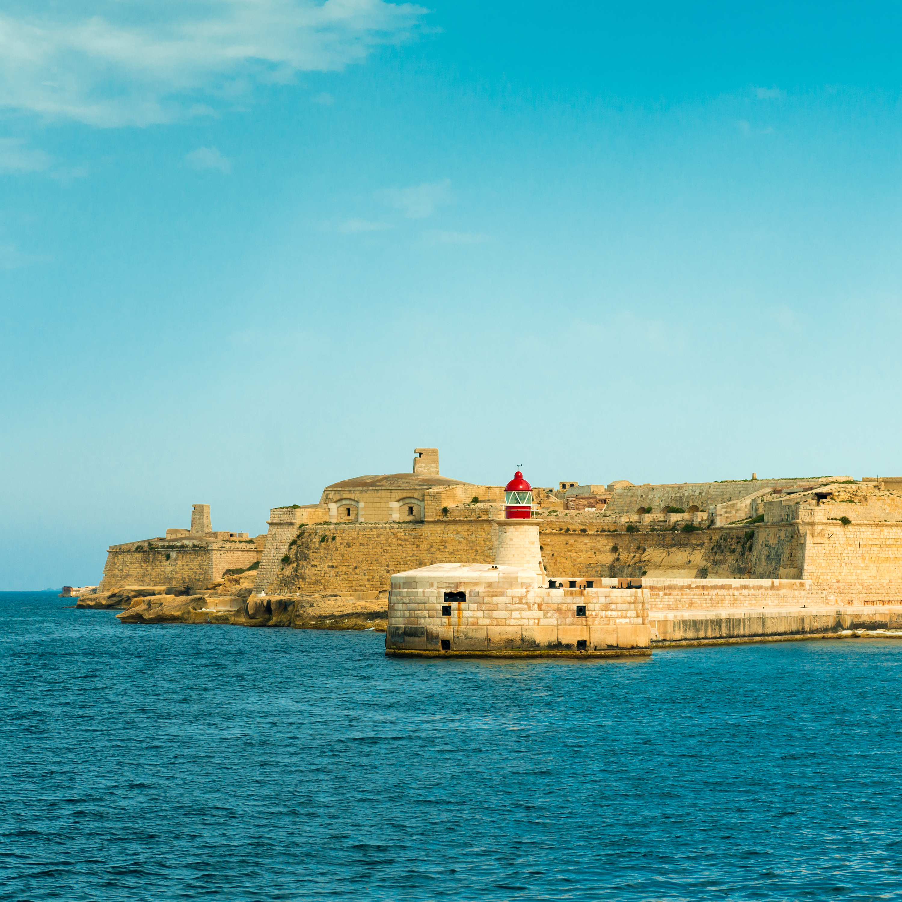 Historic fortifications and red lighthouse guarding Grand Harbour, Valletta.
