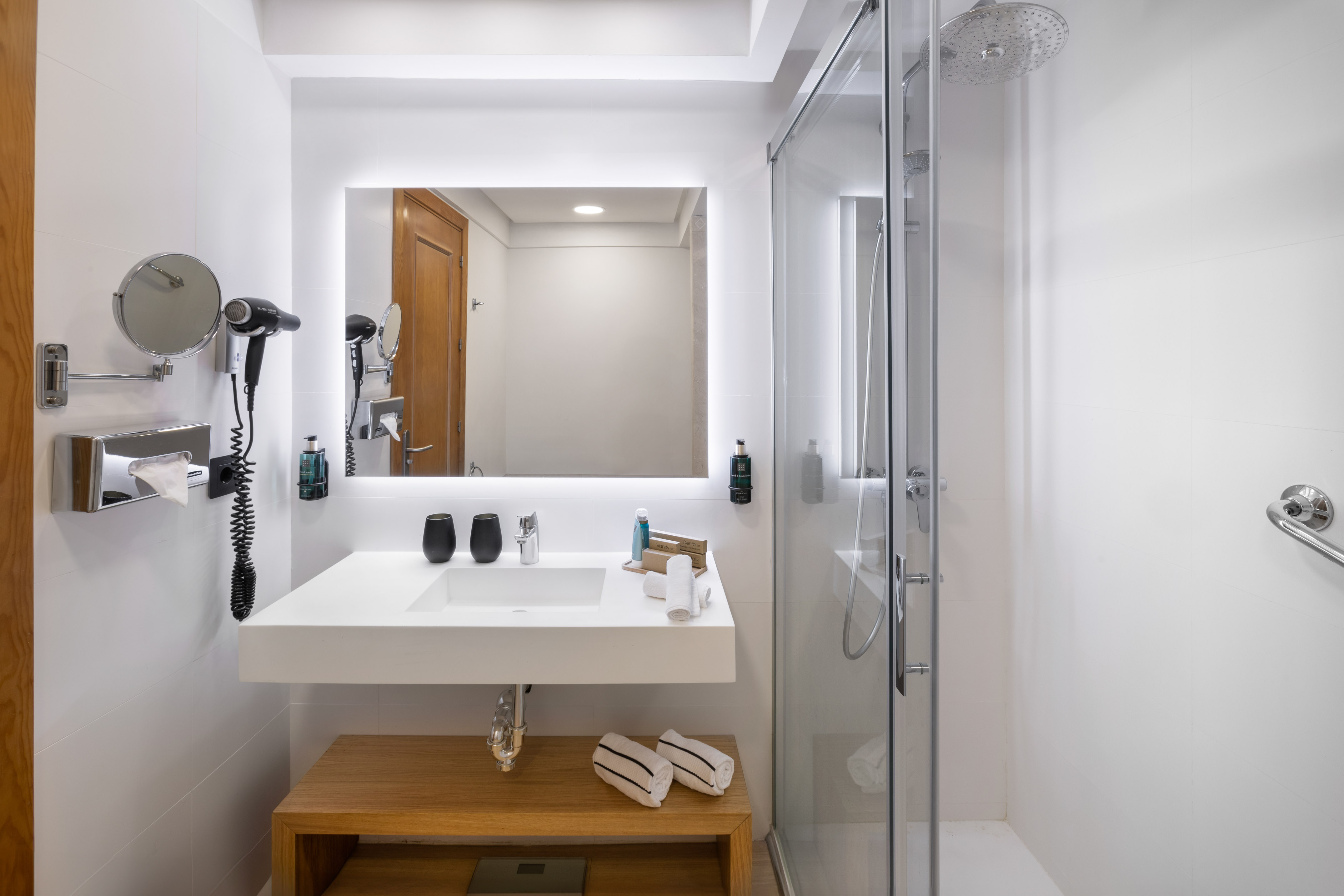 Hotel bathroom with white vanity, illuminated mirror, and glass shower.
