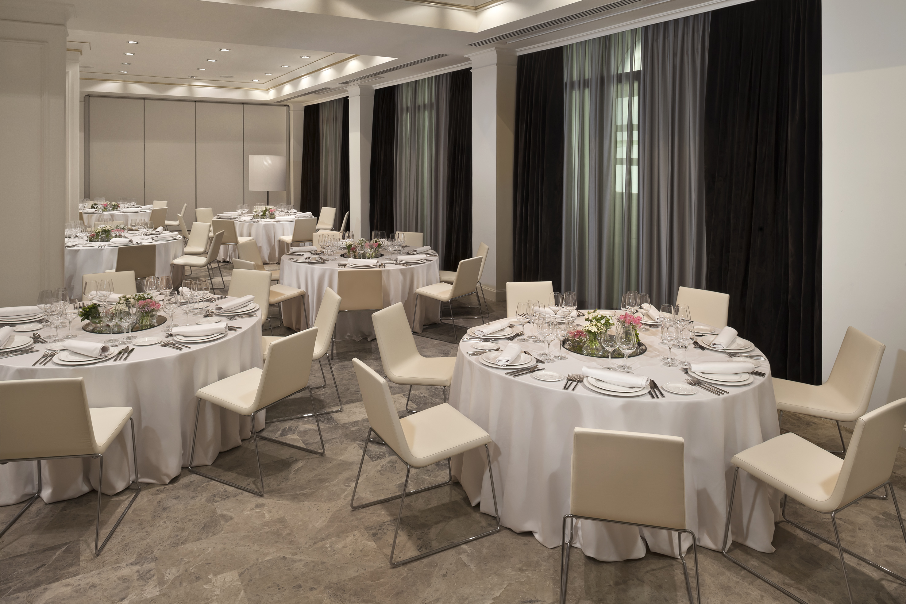 Elegant banquet hall setup with round dining tables and modern cream chairs.