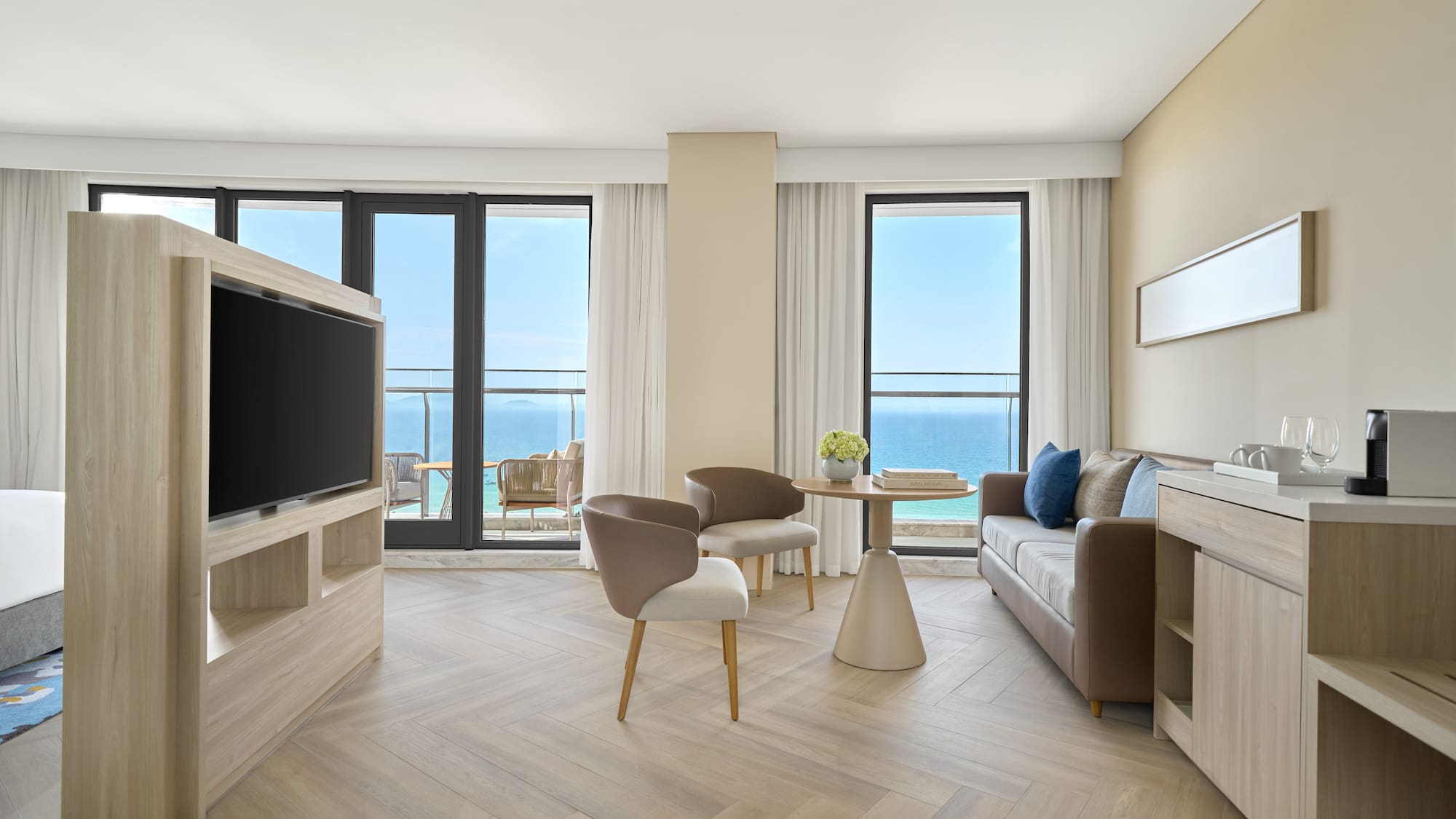 Modern hotel suite living room with ocean view balcony, sofa, and TV.
