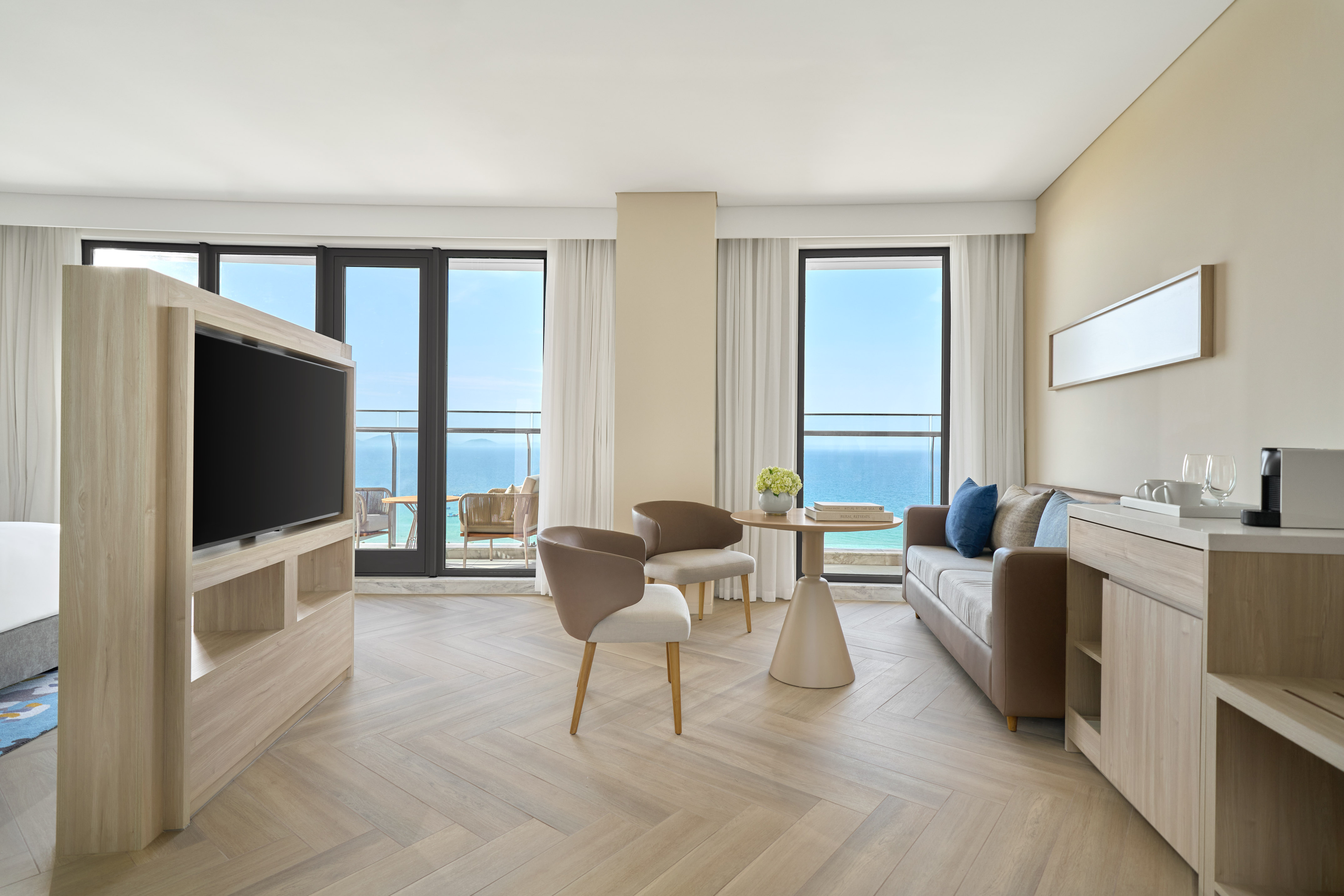 Modern hotel suite living room with ocean view balcony, sofa, and TV.