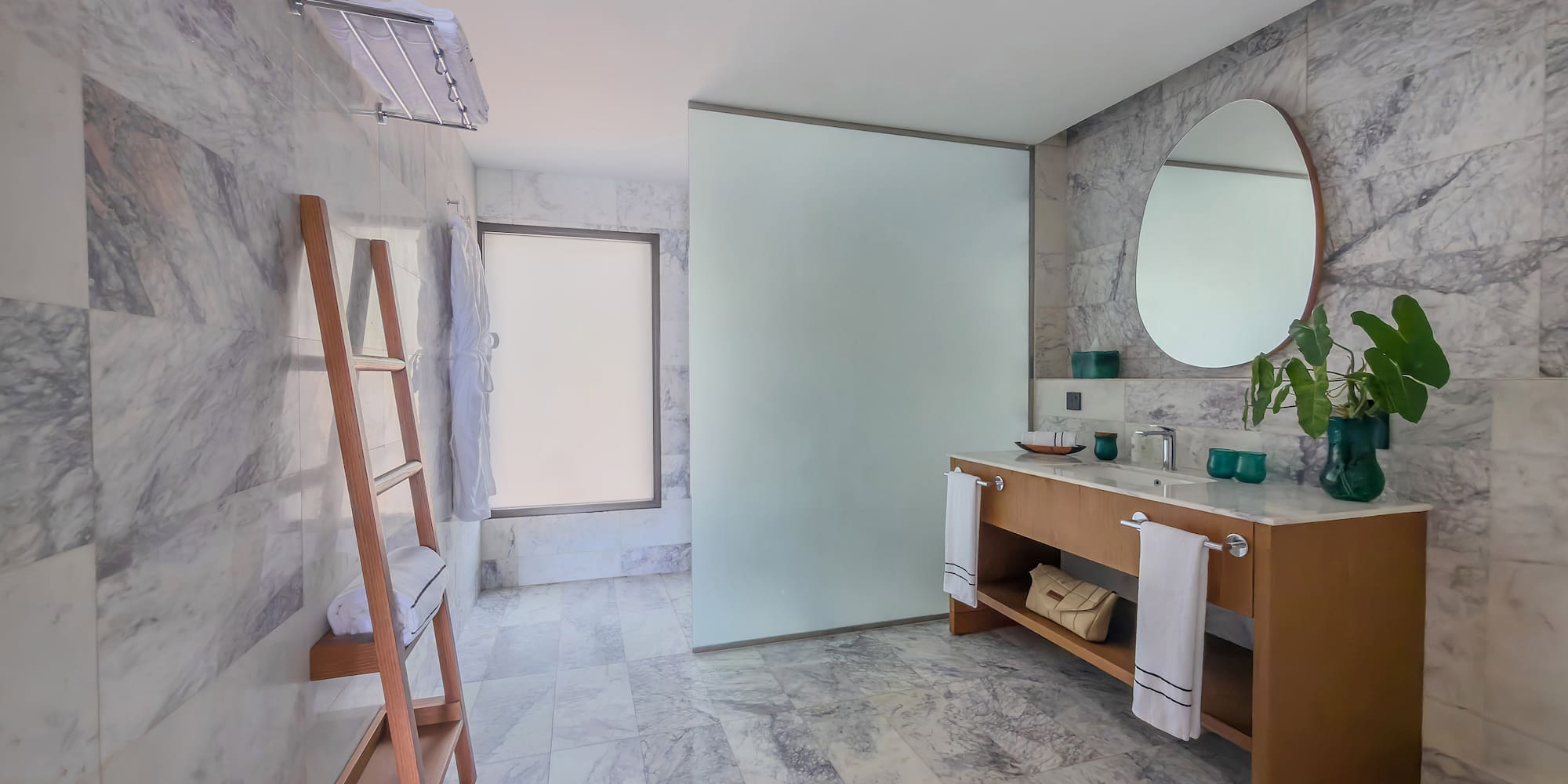 Contemporary marble bathroom with wood vanity, round mirror, and glass shower.