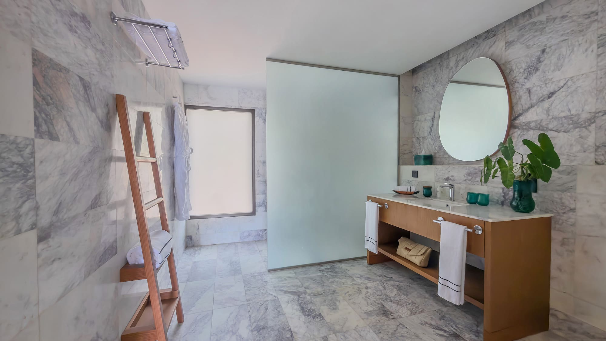 Contemporary marble bathroom with wood vanity, round mirror, and glass shower.