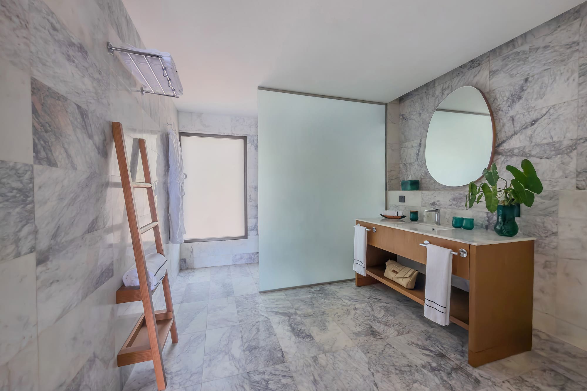 Contemporary marble bathroom with wood vanity, round mirror, and glass shower.