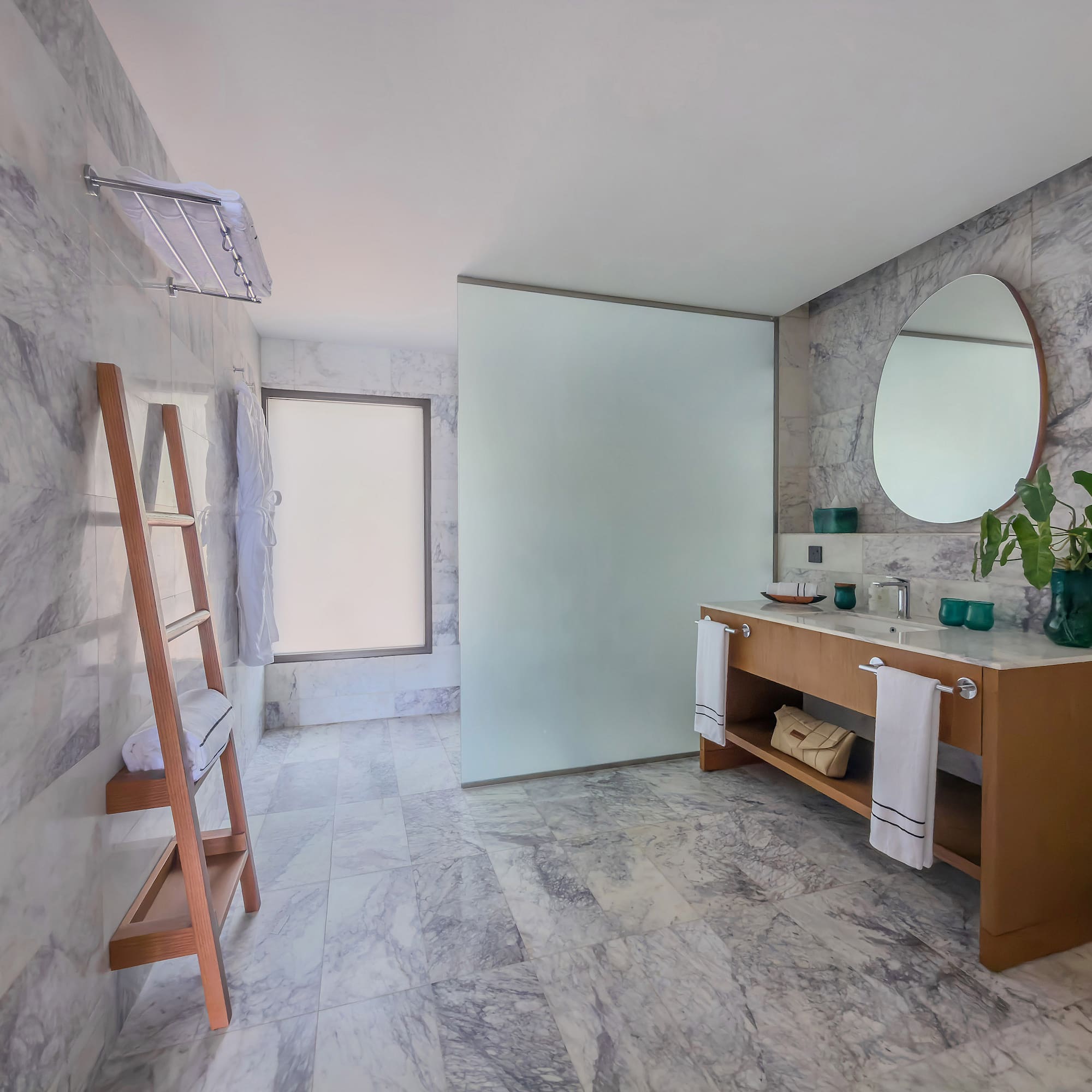 Contemporary marble bathroom with wood vanity, round mirror, and glass shower.