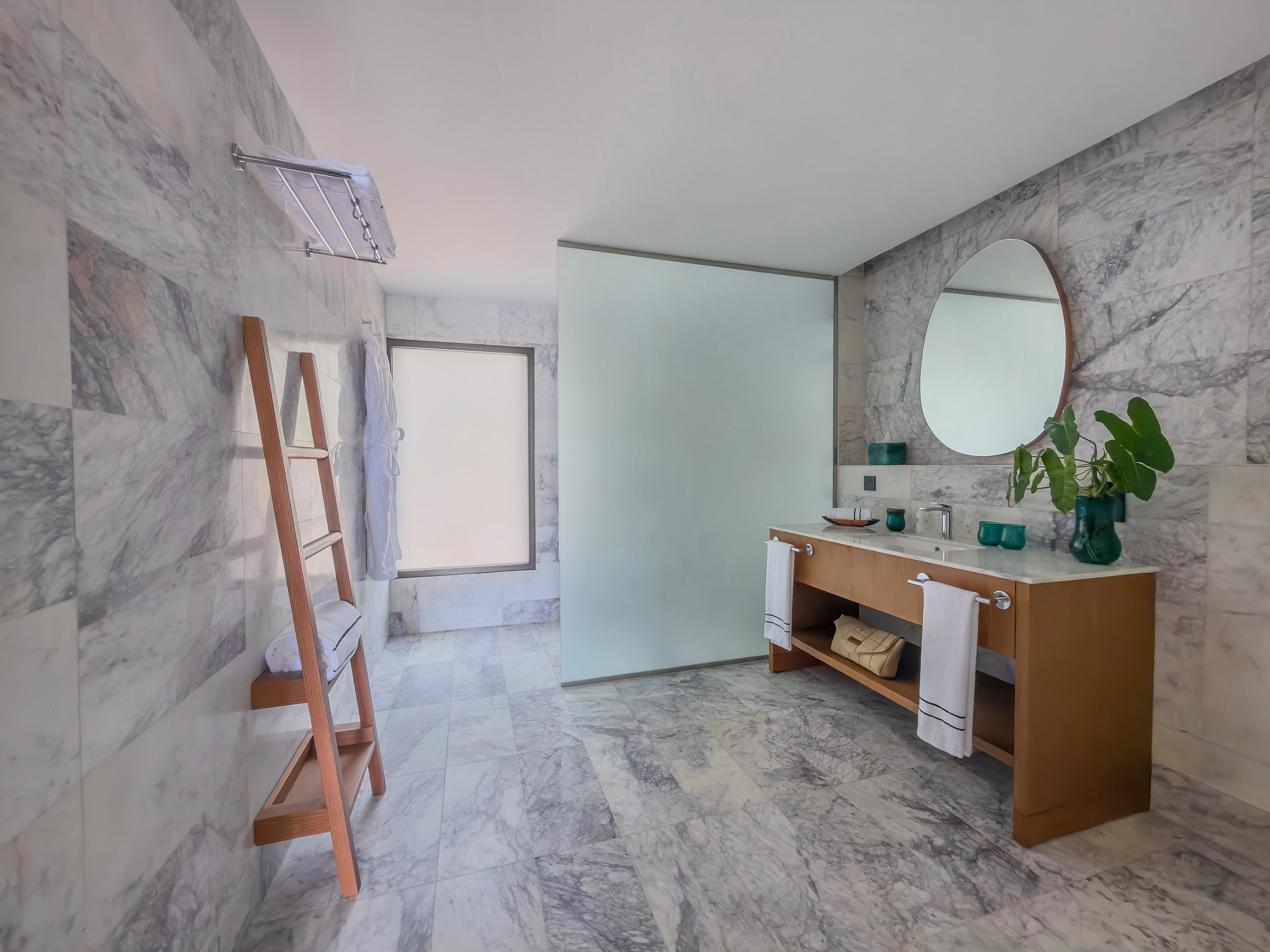 Contemporary marble bathroom with wood vanity, round mirror, and glass shower.