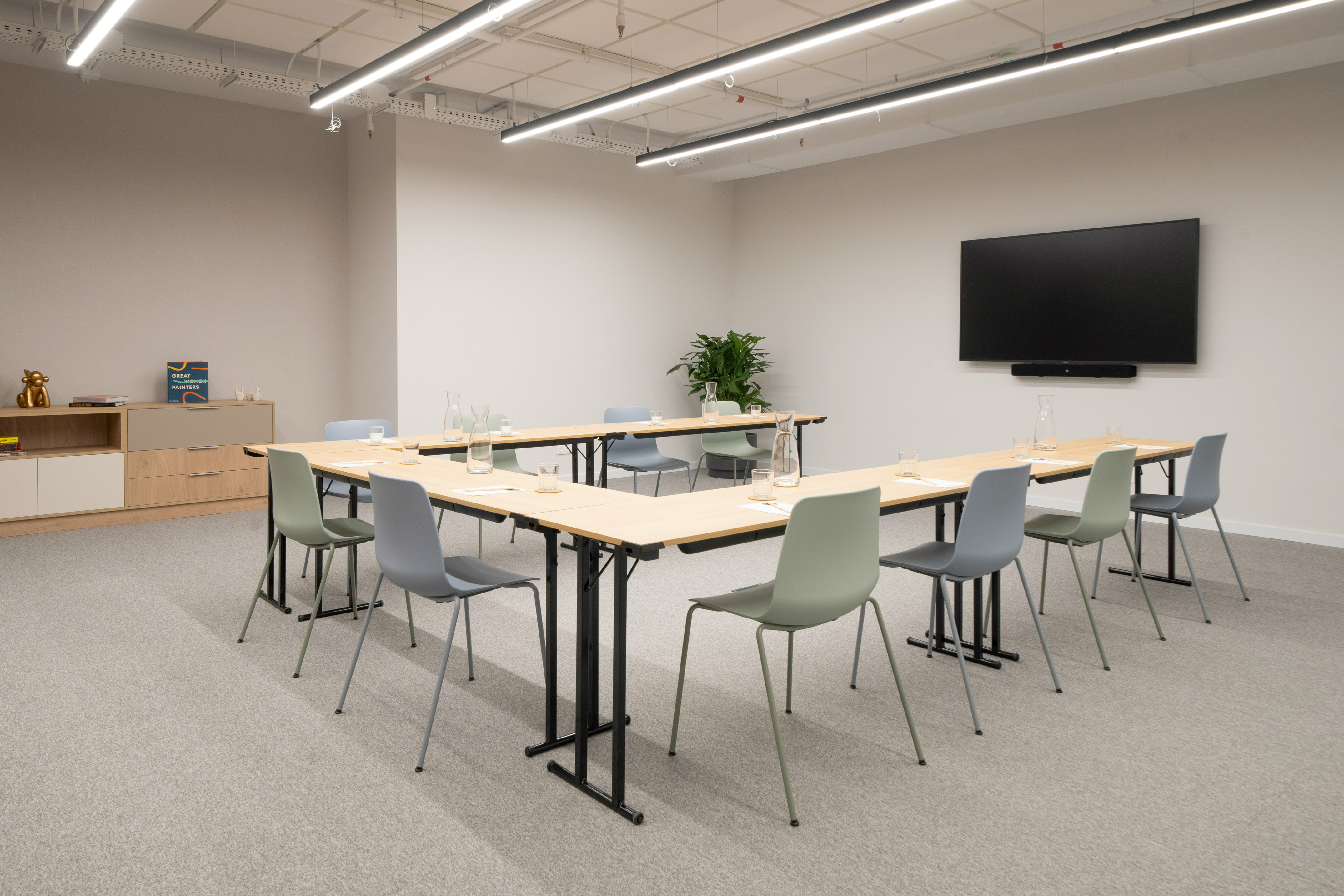 Modern meeting room with U-shaped table, green/grey chairs, and wall TV.