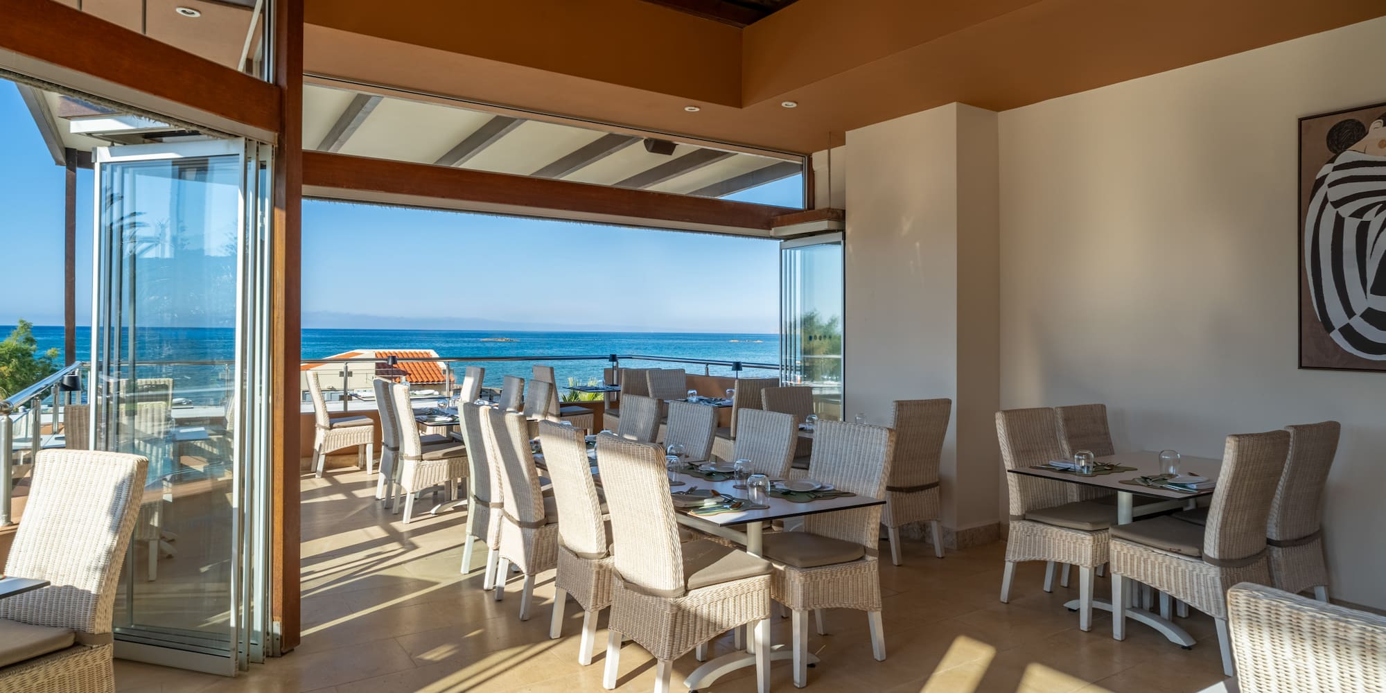 Open restaurant with ocean views, wicker dining chairs, and set tables.